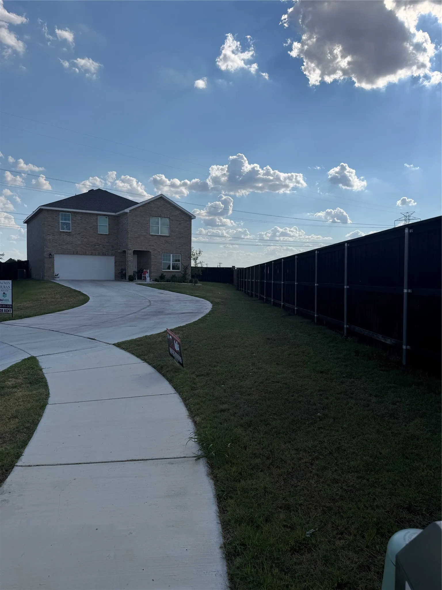 Two-story brick exterior with an attached garage, featuring a concrete driveway and sidewalk, and a dark privacy fence