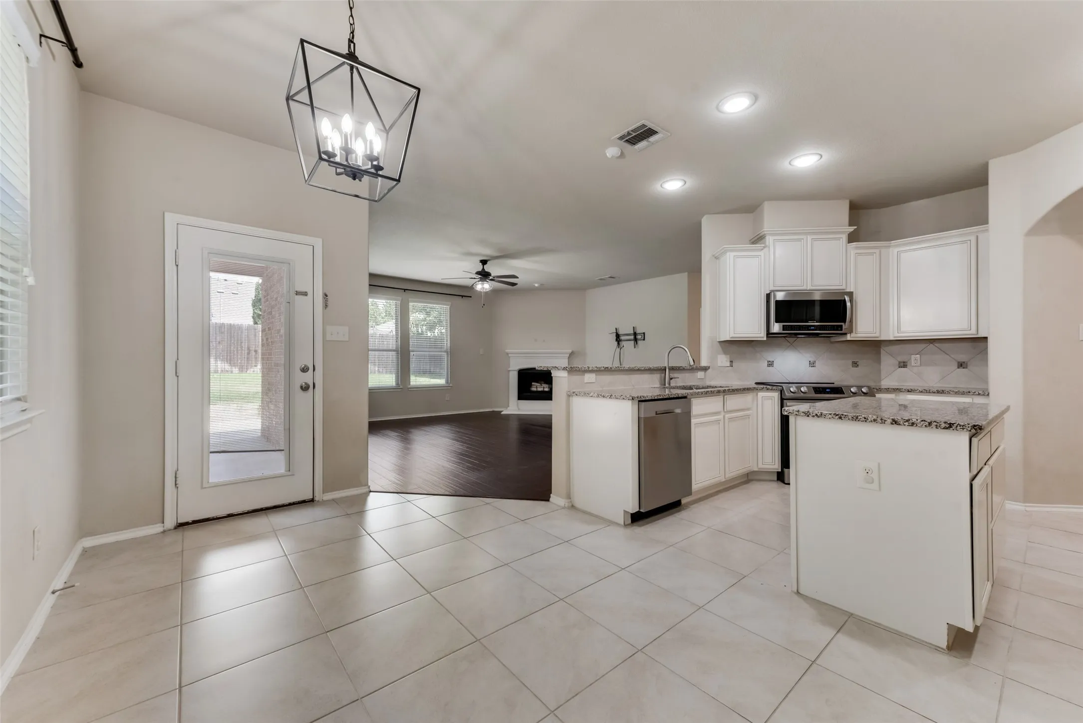Kitchen with decorative light fixtures, stainless steel appliances, ceiling fan with notable chandelier, light stone countertops, and light hardwood / wood-style flooring