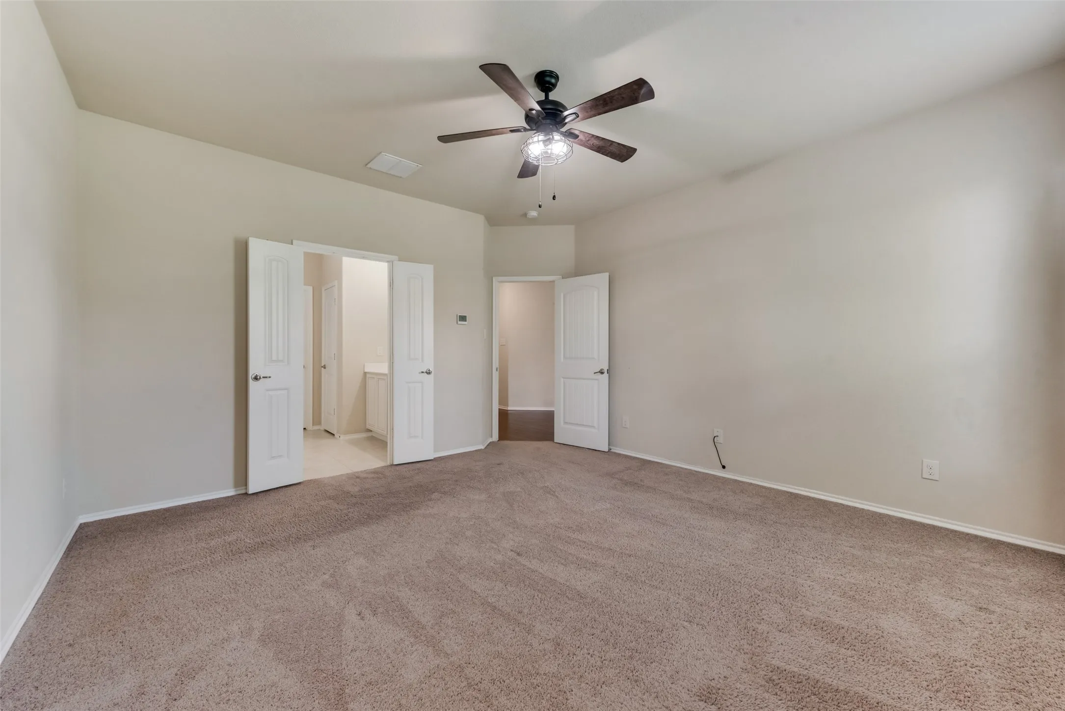Unfurnished bedroom featuring light carpet, ensuite bathroom, and ceiling fan