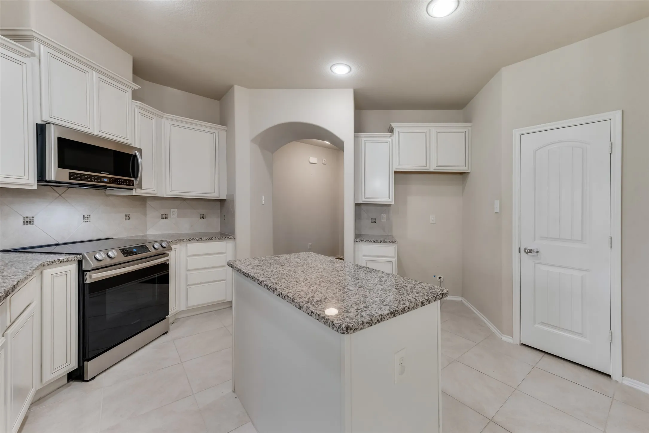 Kitchen with decorative backsplash, appliances with stainless steel finishes, white cabinets, and a center island