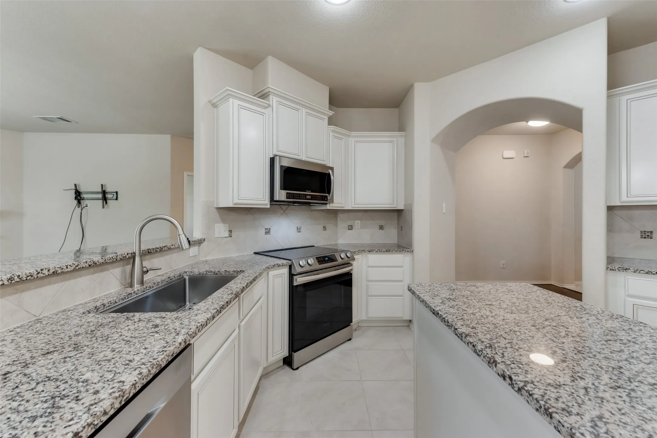 Kitchen featuring white cabinetry, tasteful backsplash, stainless steel appliances, light stone countertops, and sink