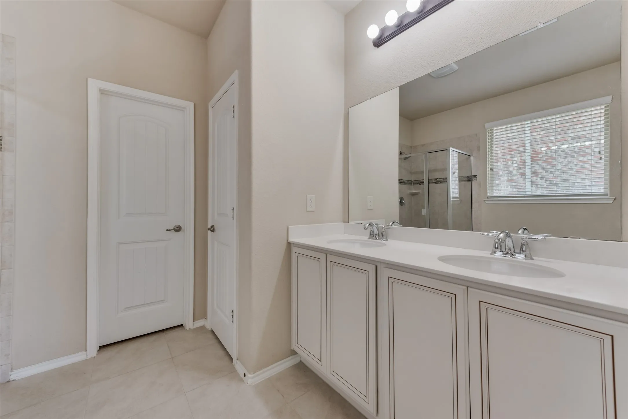 Bathroom with a shower with shower door, tile patterned flooring, and double vanity