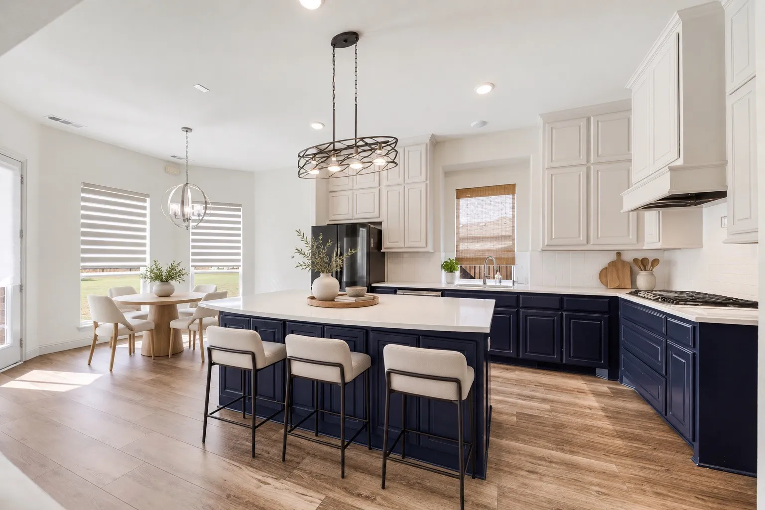 Spacious kitchen featuring two-tone cabinetry, a large center island with seating, wood-finish flooring, and a dining area with multiple windows staging with AI