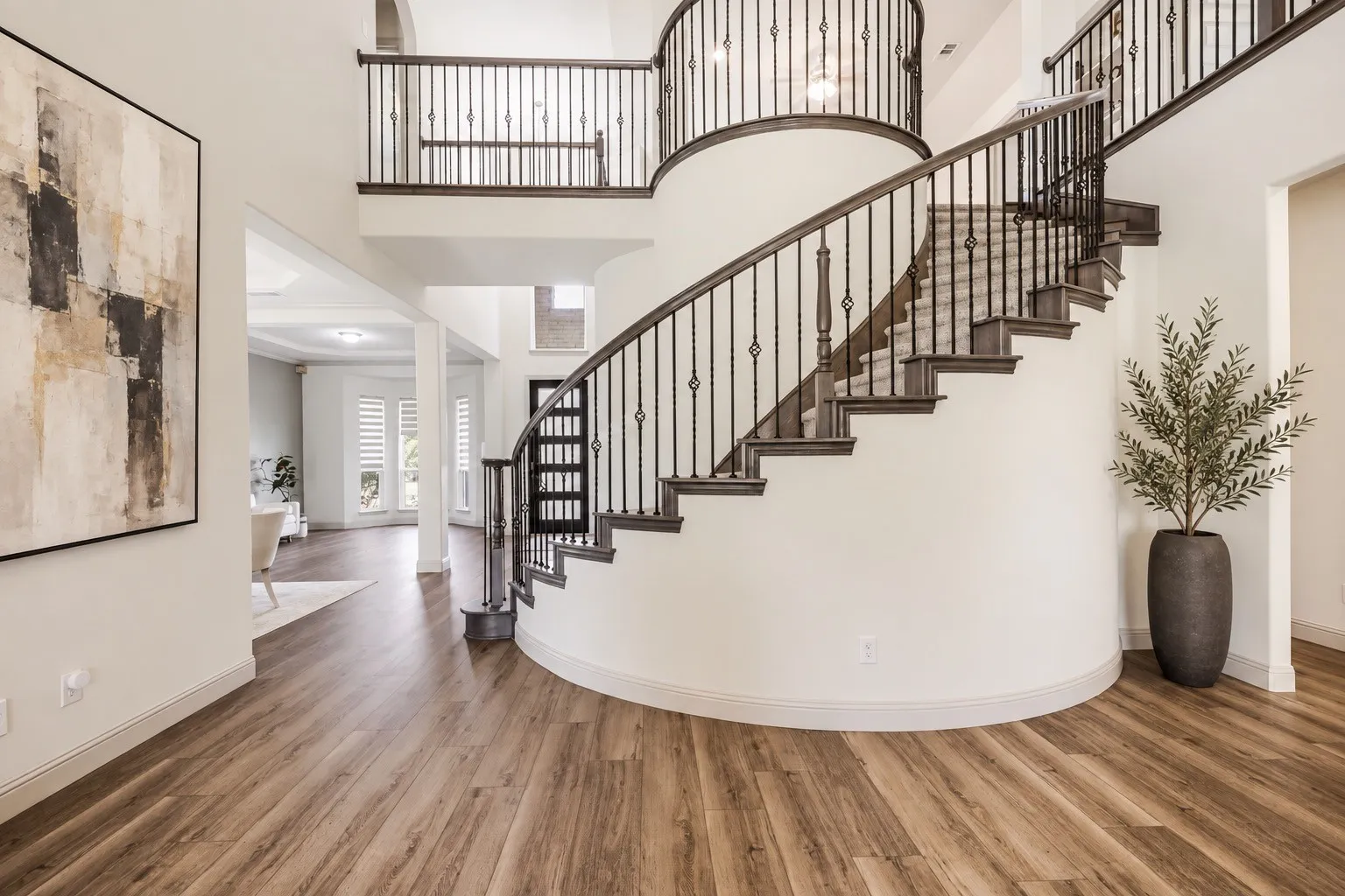 Curved staircase with wrought iron balusters, wood-finish flooring, and a two-story entryway- staging with AI
