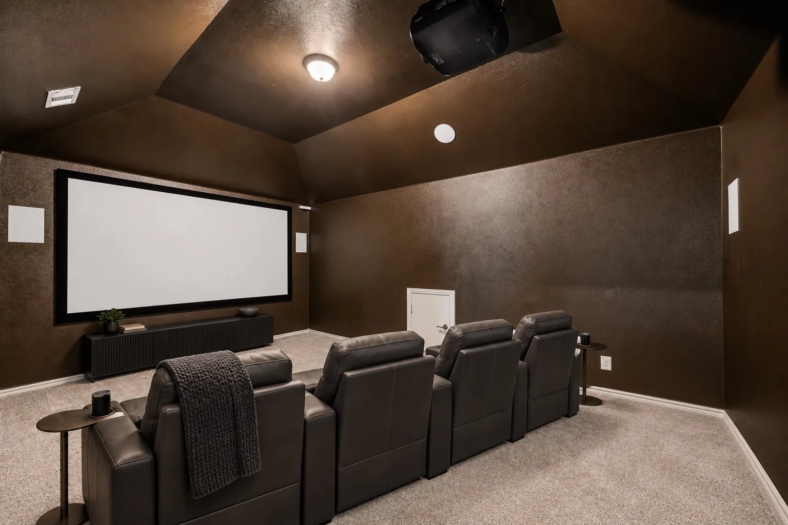 Dedicated media room with vaulted ceilings, a large projection screen, recessed projector, and in-wall speakers staging with AI