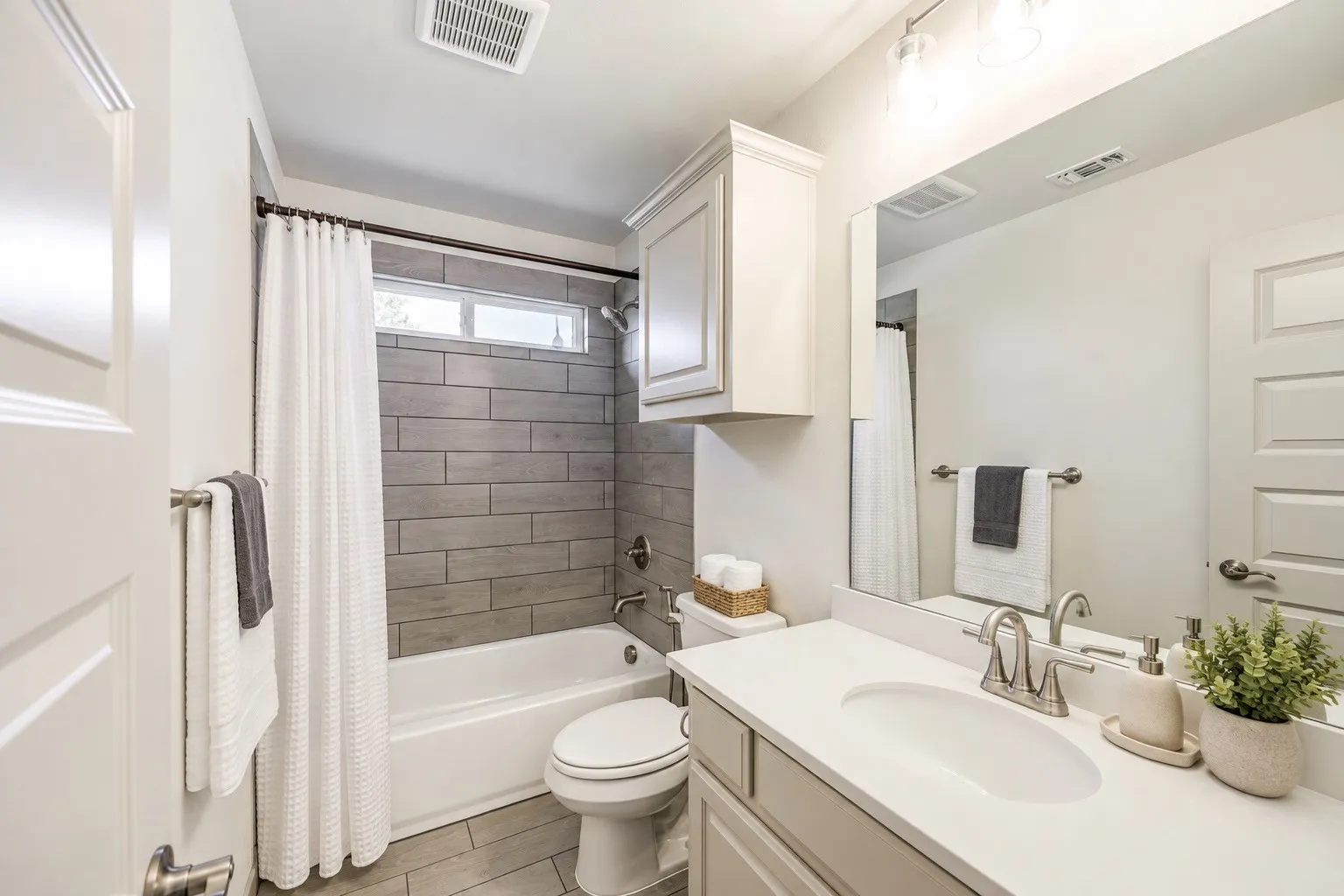 Bathroom featuring a full-sized bathtub with subway tile surround, a single vanity with an integrated sink, a wall-mounted mirror, and an overhead storage cabinet staging with AI