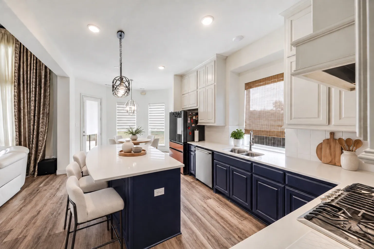 Open-concept kitchen with a large central island, contrasting dark and light cabinetry, a gas cooktop, and wood-finish flooring- staging with AI