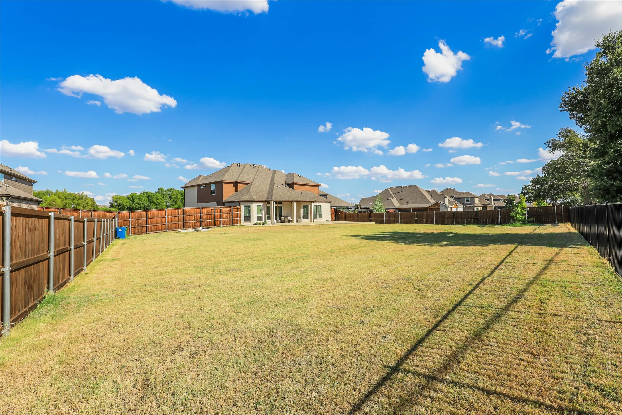 Expansive backyard featuring a manicured lawn, a full wood privacy fence, and a covered patio with pillars