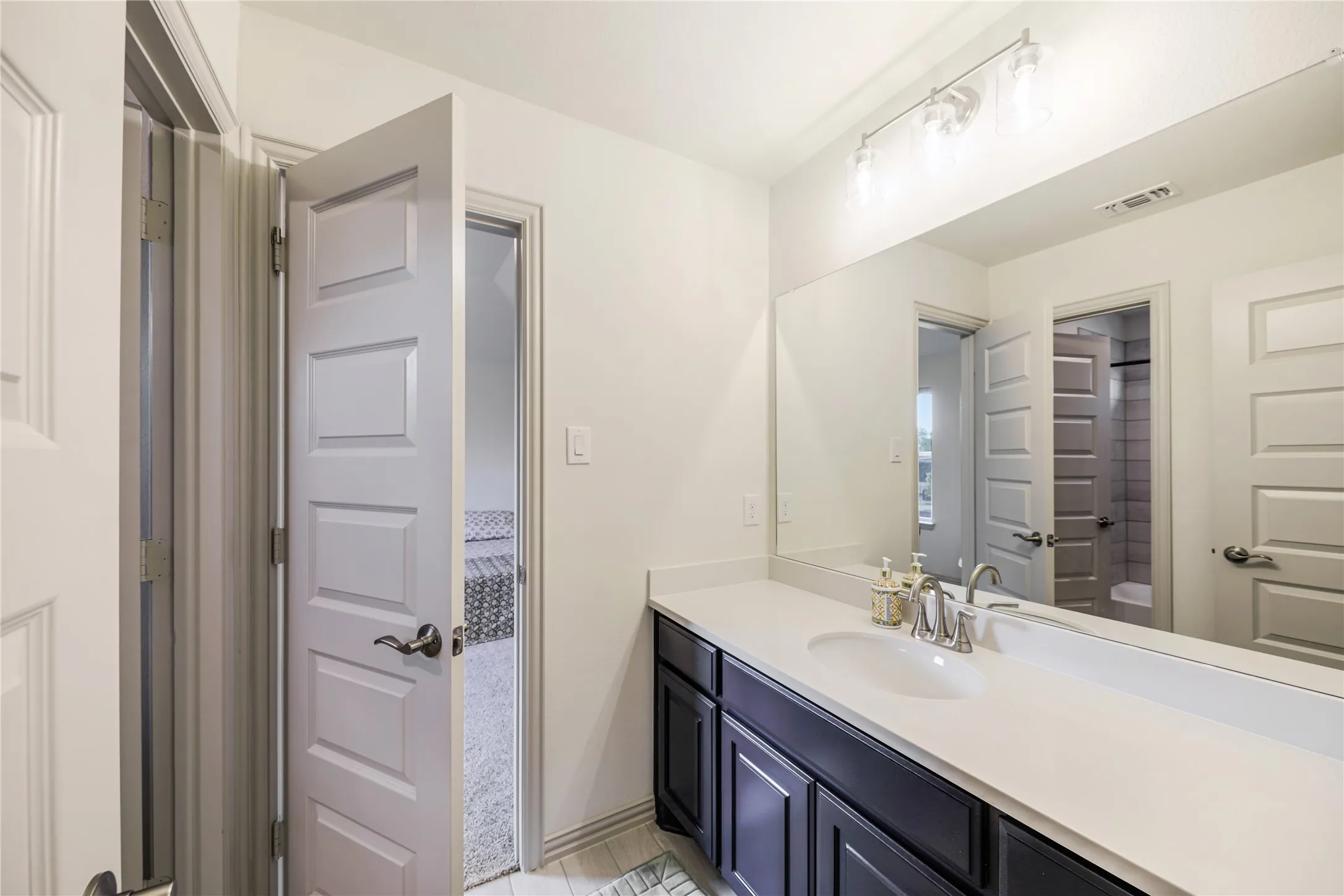 White vanity with a single basin, stainless steel faucet, and overhead track lighting
