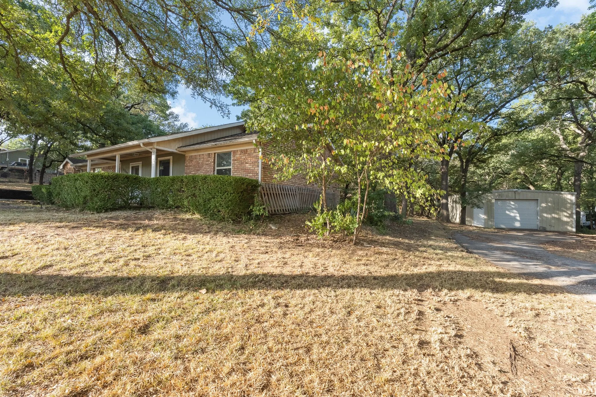 Brick exterior home with a covered front porch, mature trees, and a detached two-car garage