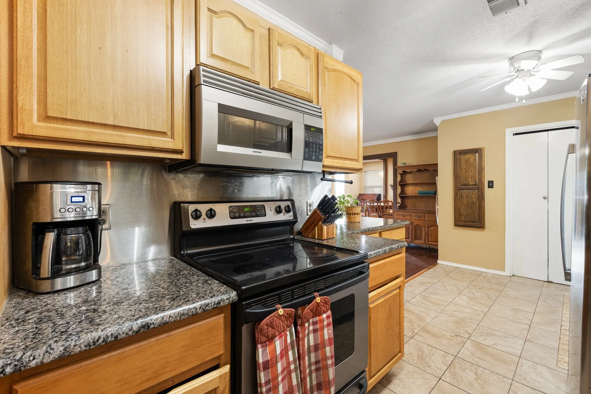 Kitchen featuring light wood cabinetry, stainless steel appliances, granite-look countertops, a stainless steel backsplash, and tile flooring