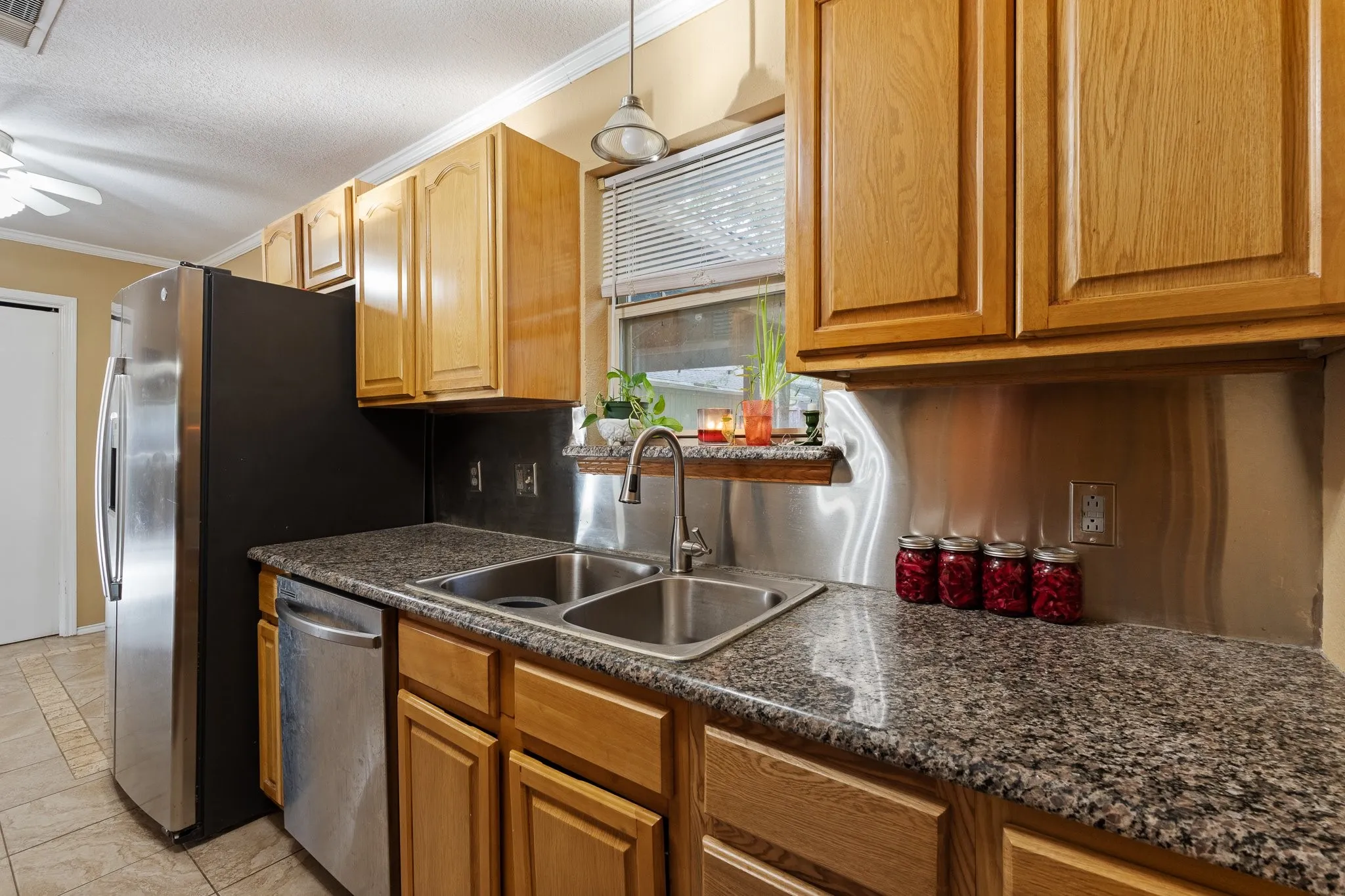 Kitchen featuring wood cabinetry, a stainless steel double basin sink, stainless steel backsplash, and a built-in dishwasher