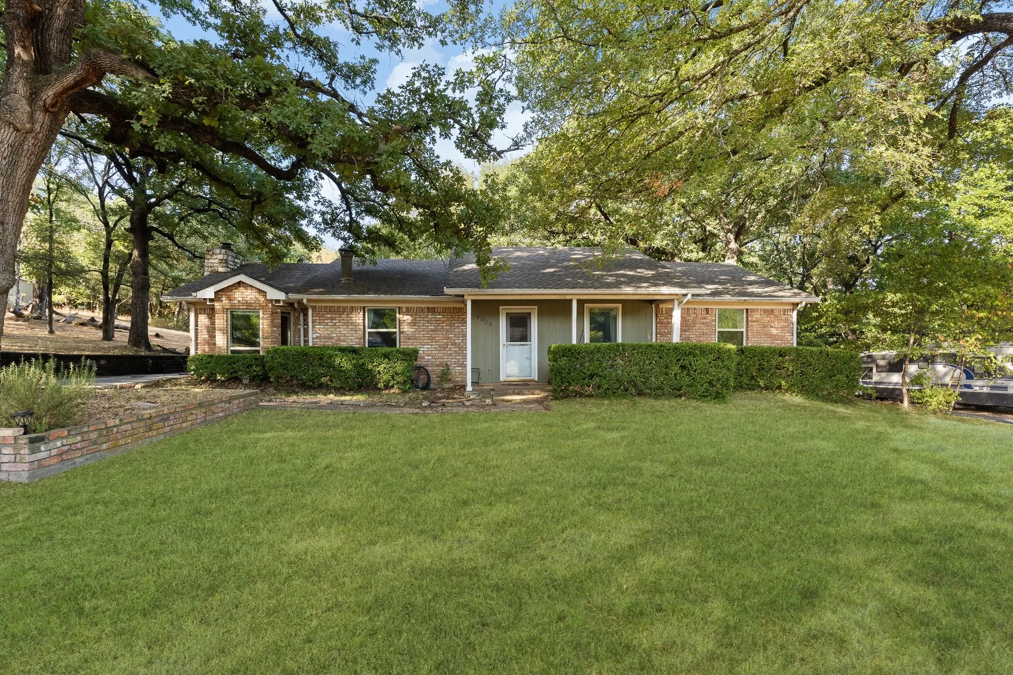 Brick exterior with a covered entry, mature landscaping, and a substantial front lawn