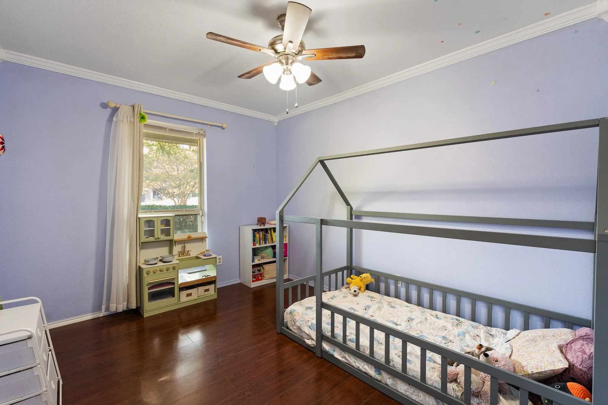 Wood-finish flooring, single window with sheer curtain, ceiling fan with light fixture, and white crown molding