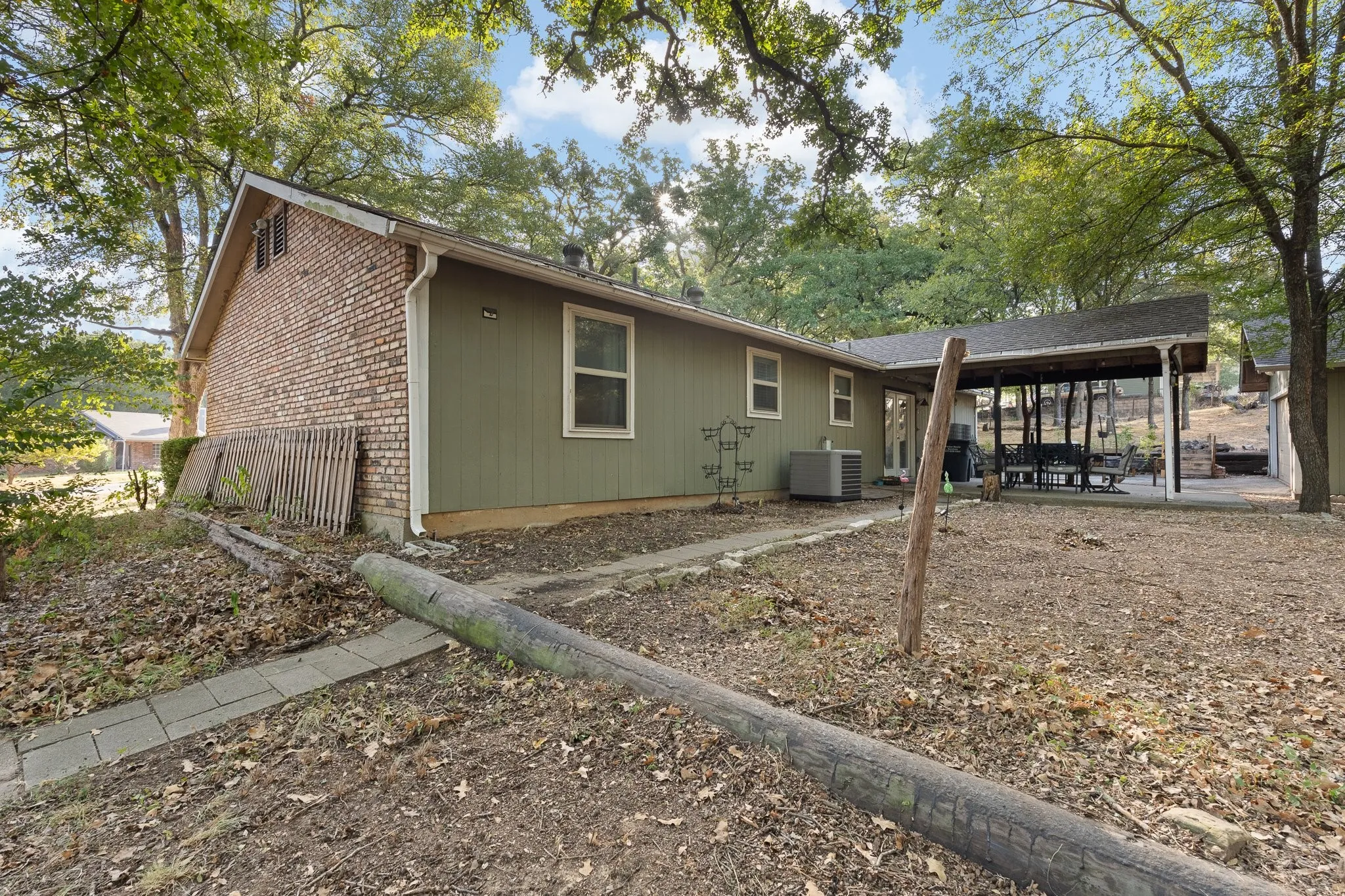 Brick and siding exterior with a covered patio area, mature trees