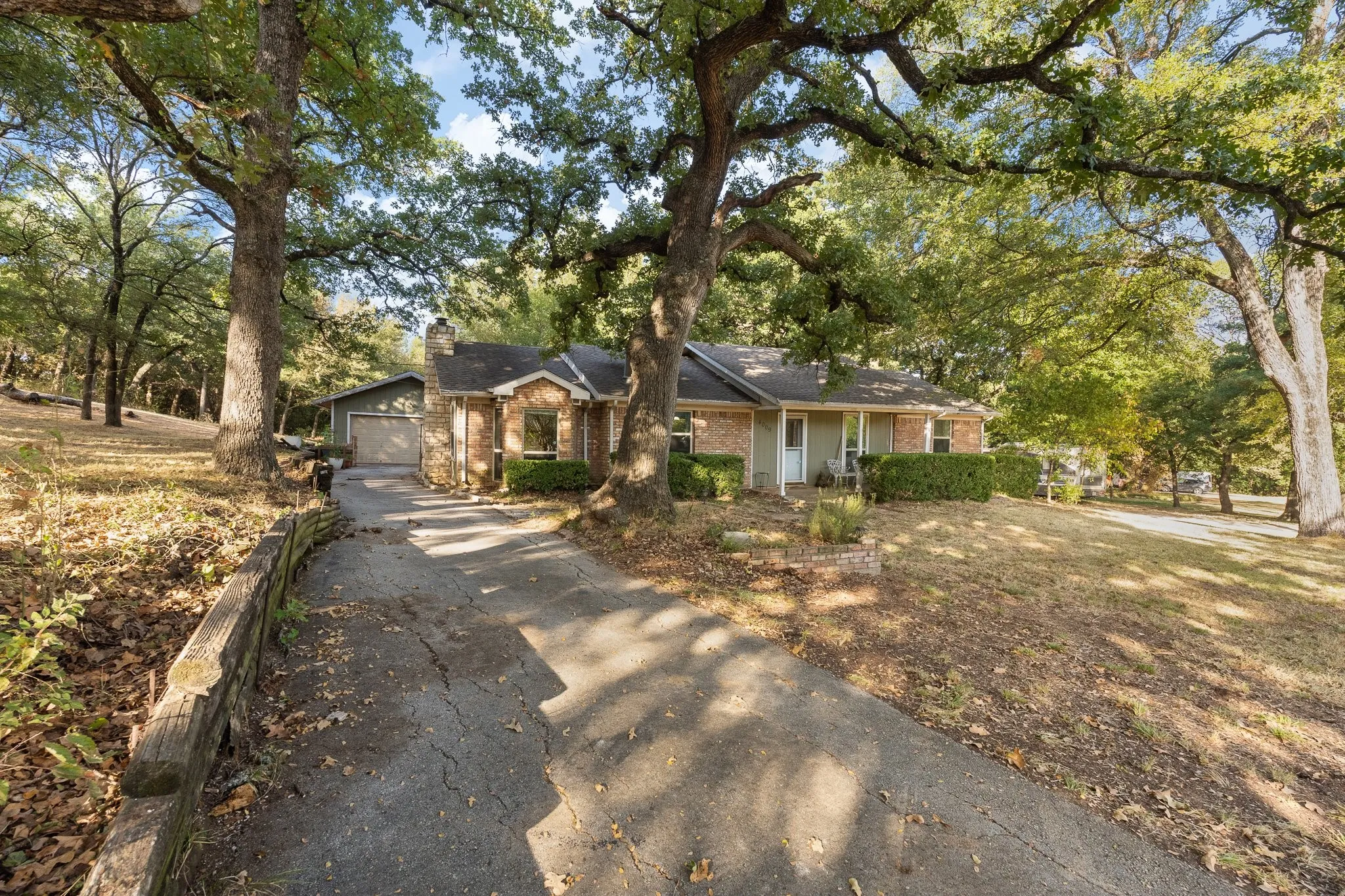 Brick facade home with a covered front porch, attached garage, stone chimney, and mature trees