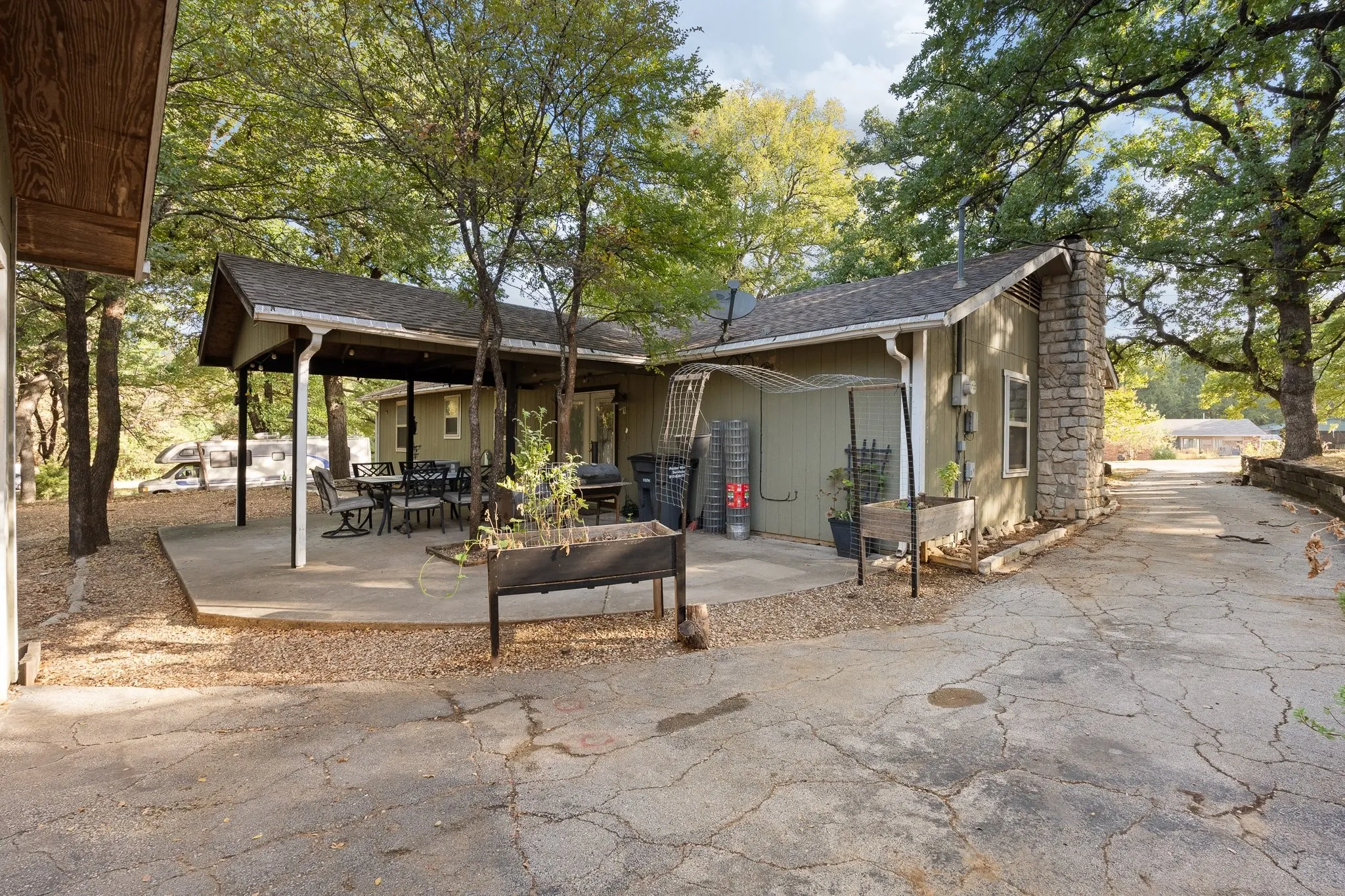 Covered patio with a concrete slab, stone chimney, and mature trees