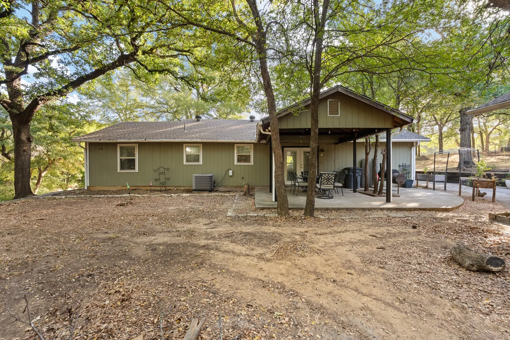 Expansive outdoor space featuring a covered patio, additional concrete pad, and mature trees