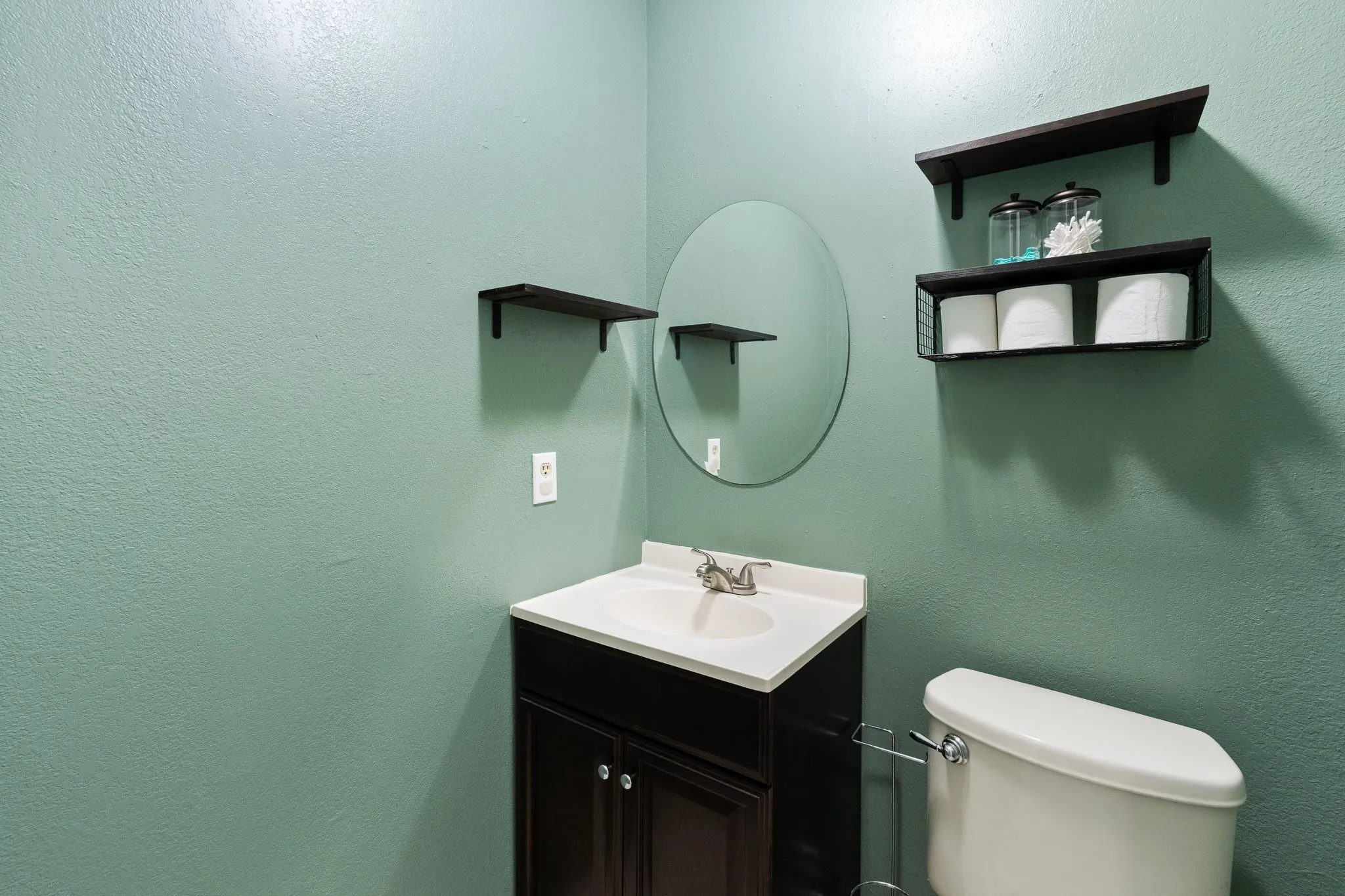 Bathroom featuring a dark wood-finish vanity with an integrated white sink, a chrome-finish faucet, an oval wall-mounted mirror
