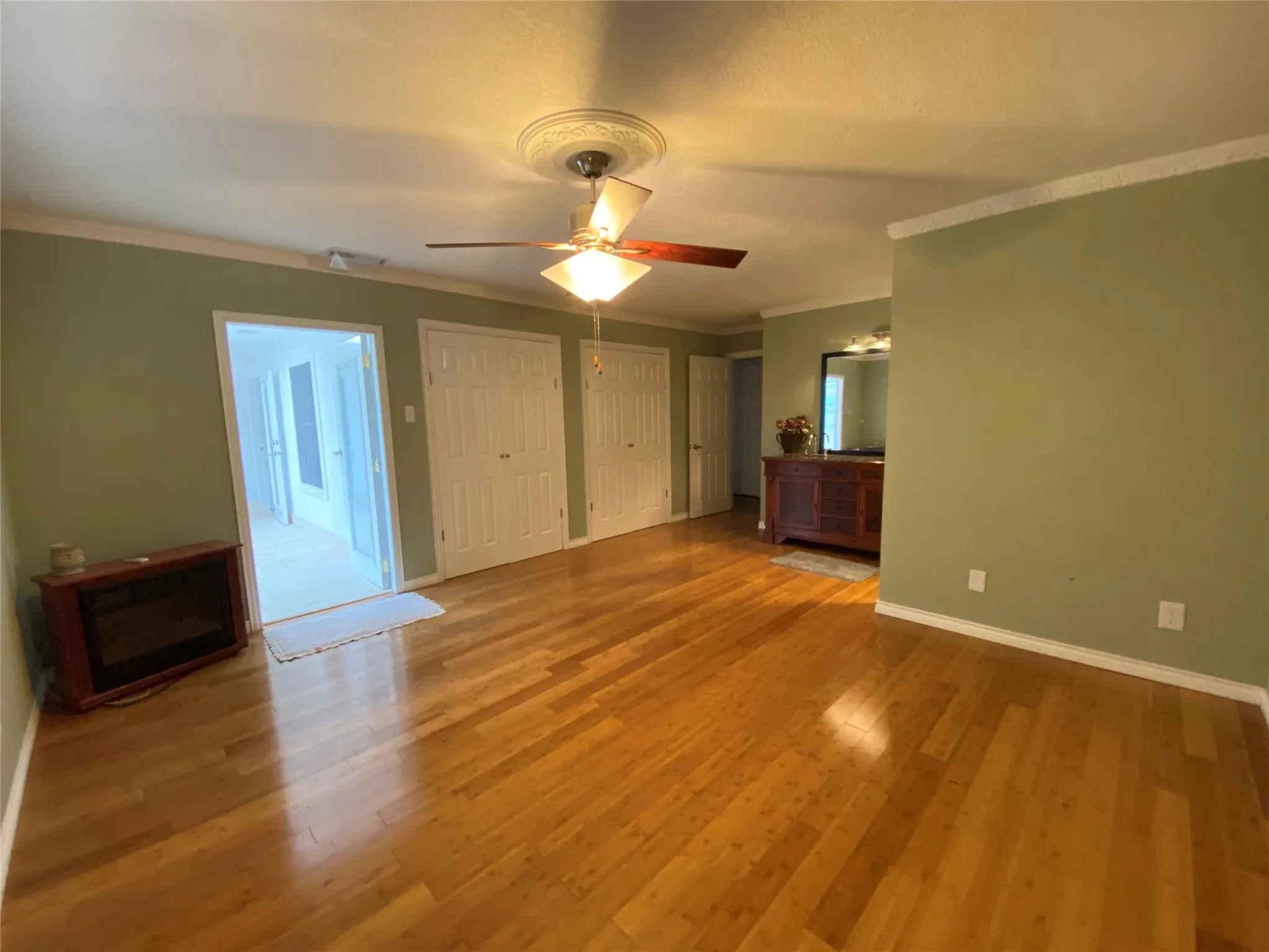 Unfurnished bedroom featuring ornamental molding, wood finished floors, multiple closets, baseboards, and ceiling fan