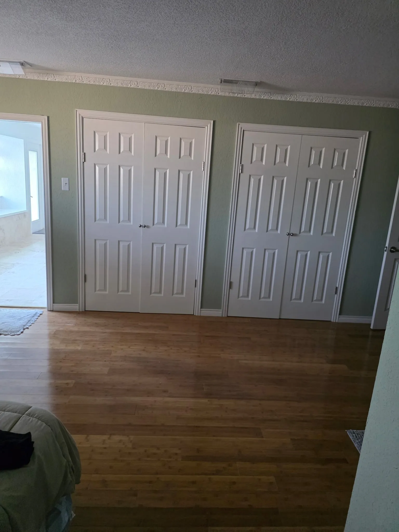 Unfurnished bedroom featuring a textured ceiling, baseboards, multiple closets, and wood finished floors