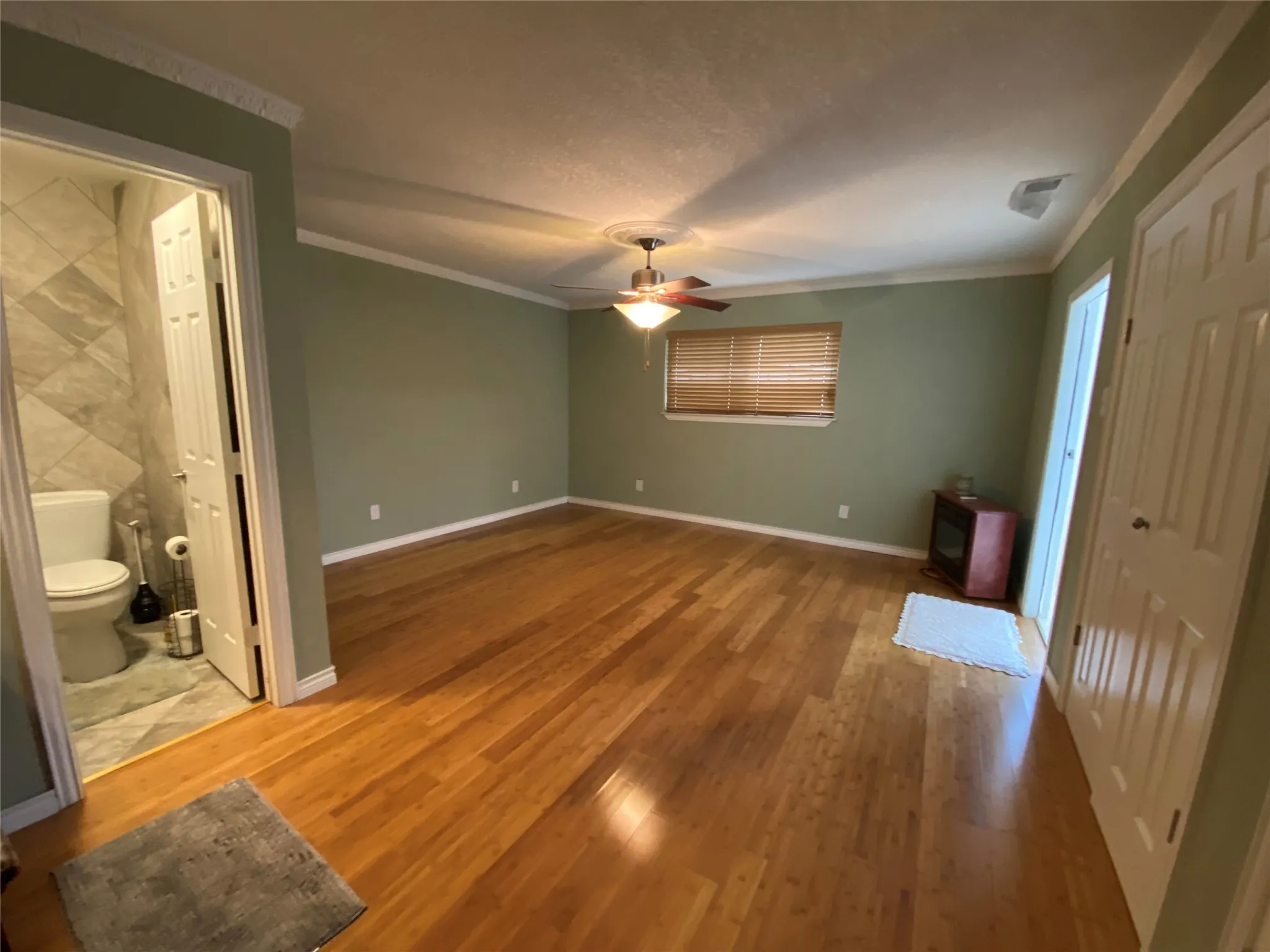 Unfurnished bedroom with ornamental molding, wood finished floors, baseboards, ceiling fan, and connected bathroom