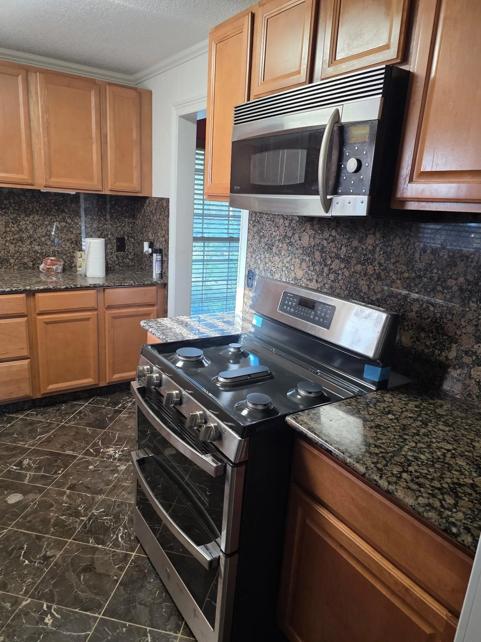 Kitchen featuring dark stone counters, appliances with stainless steel finishes, marble finish floor, and tasteful backsplash