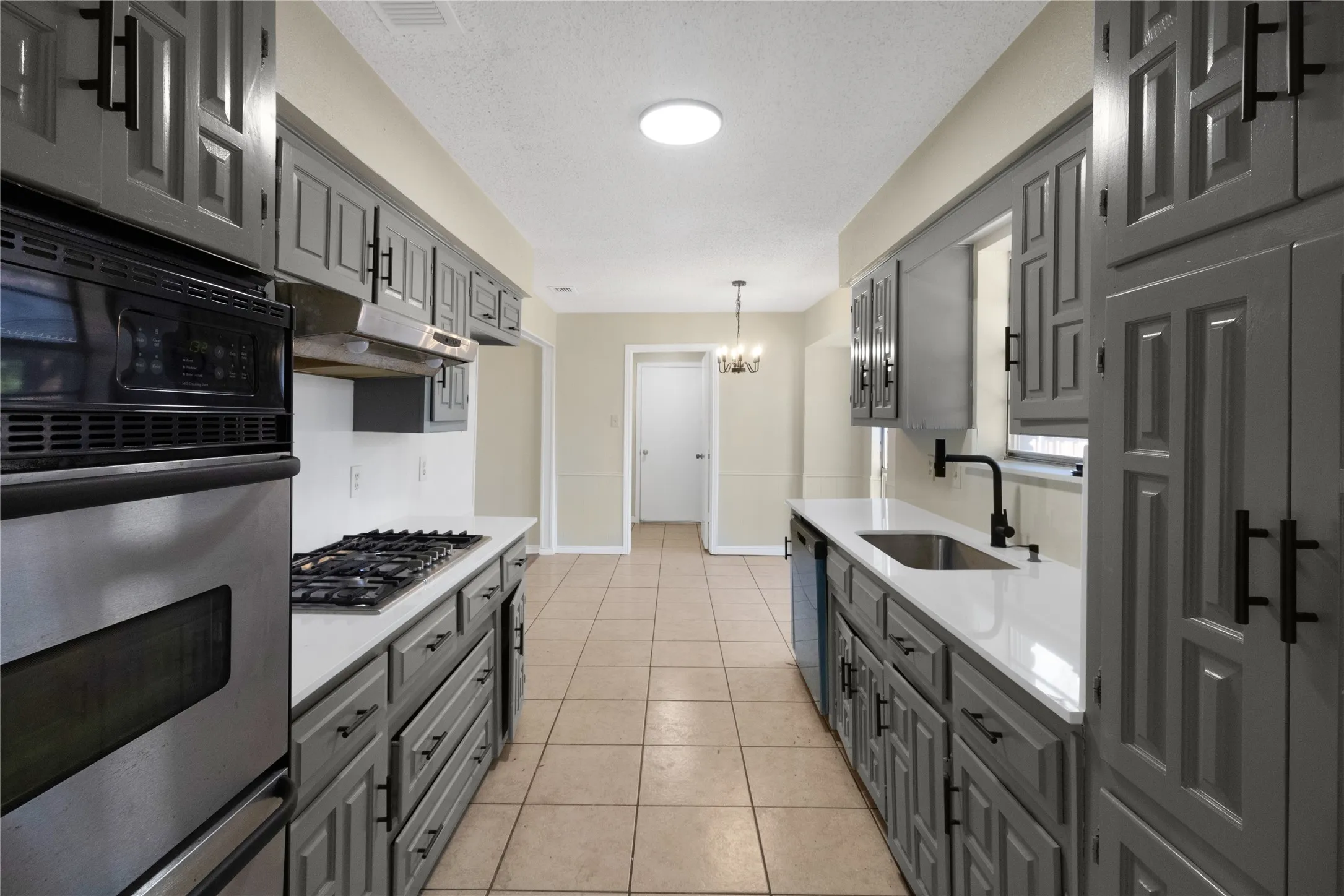 Galley kitchen featuring gray cabinetry, stainless steel appliances, light-toned tile flooring, and a circular ceiling light fixture