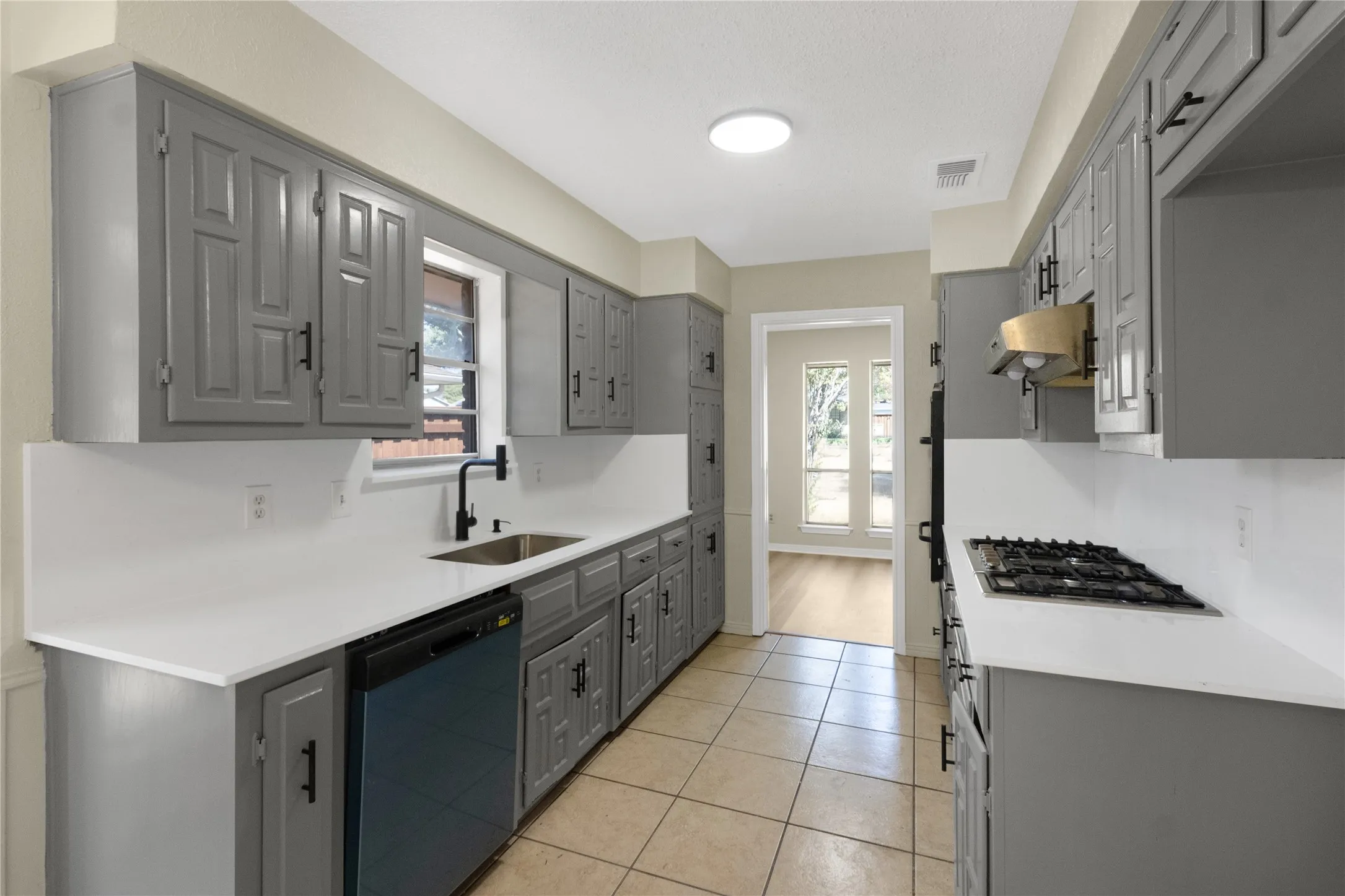 Well-appointed kitchen featuring gray paneled cabinetry, light-toned countertops, a stainless steel sink with a matte black faucet, and a built-in gas cooktop