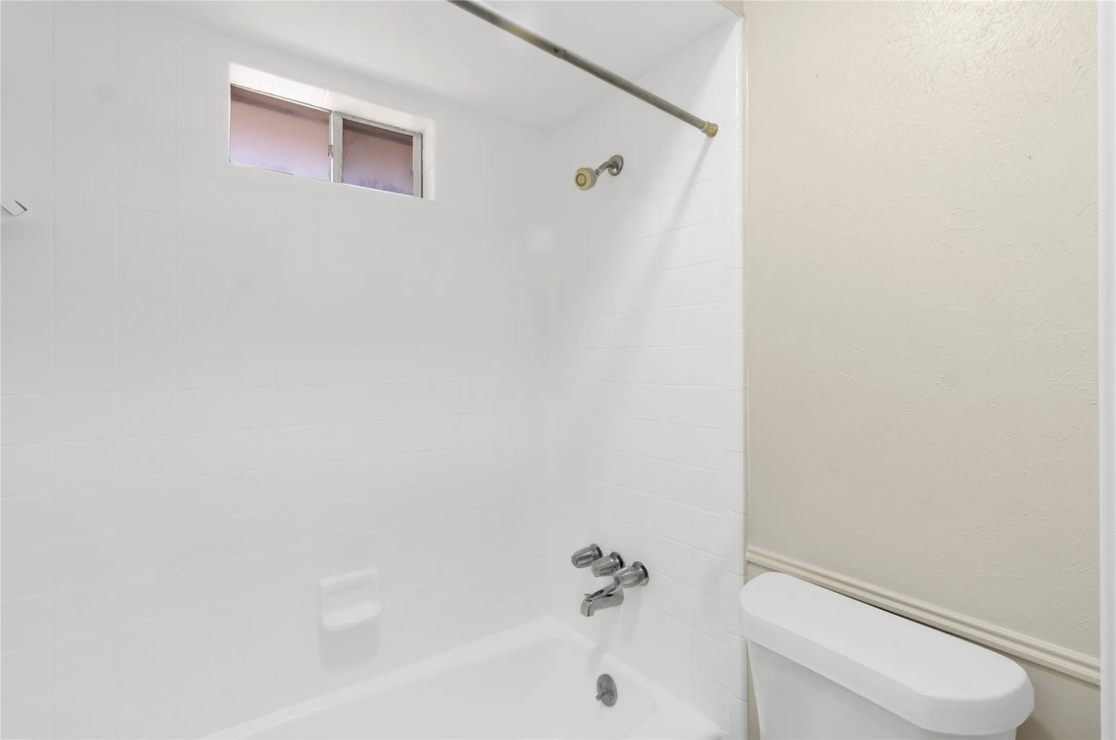 Bathtub with a white tiled surround, chrome fixtures, and a high-set window
