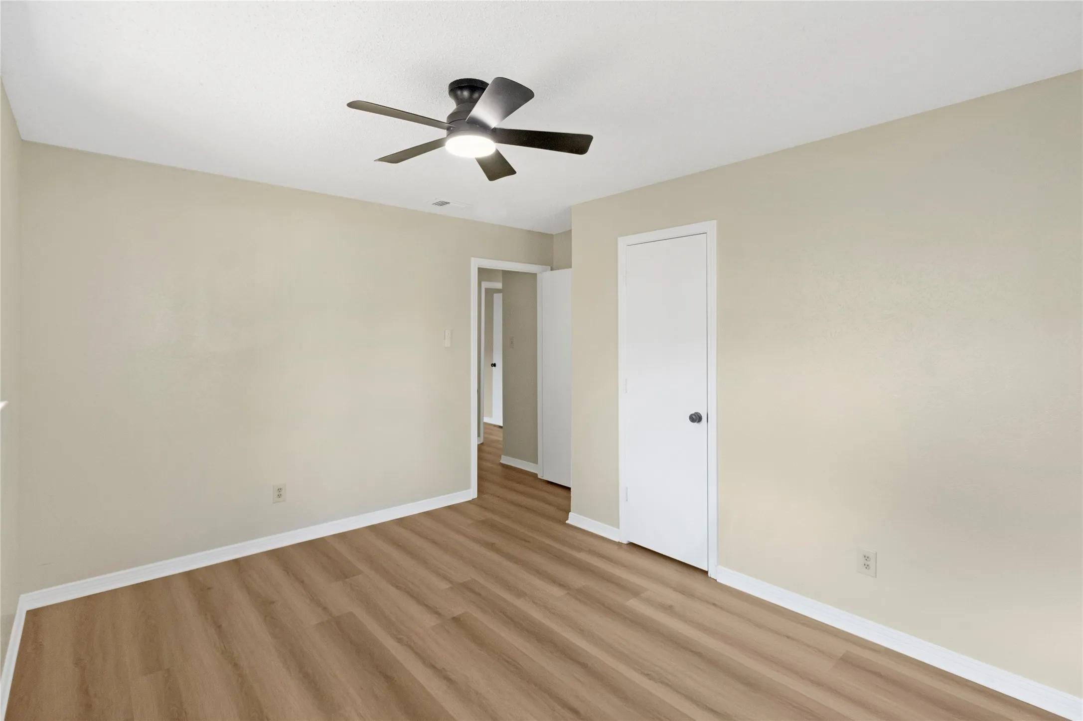 Wood-finish flooring with neutral wall tones and a ceiling-mounted fan with integrated lighting