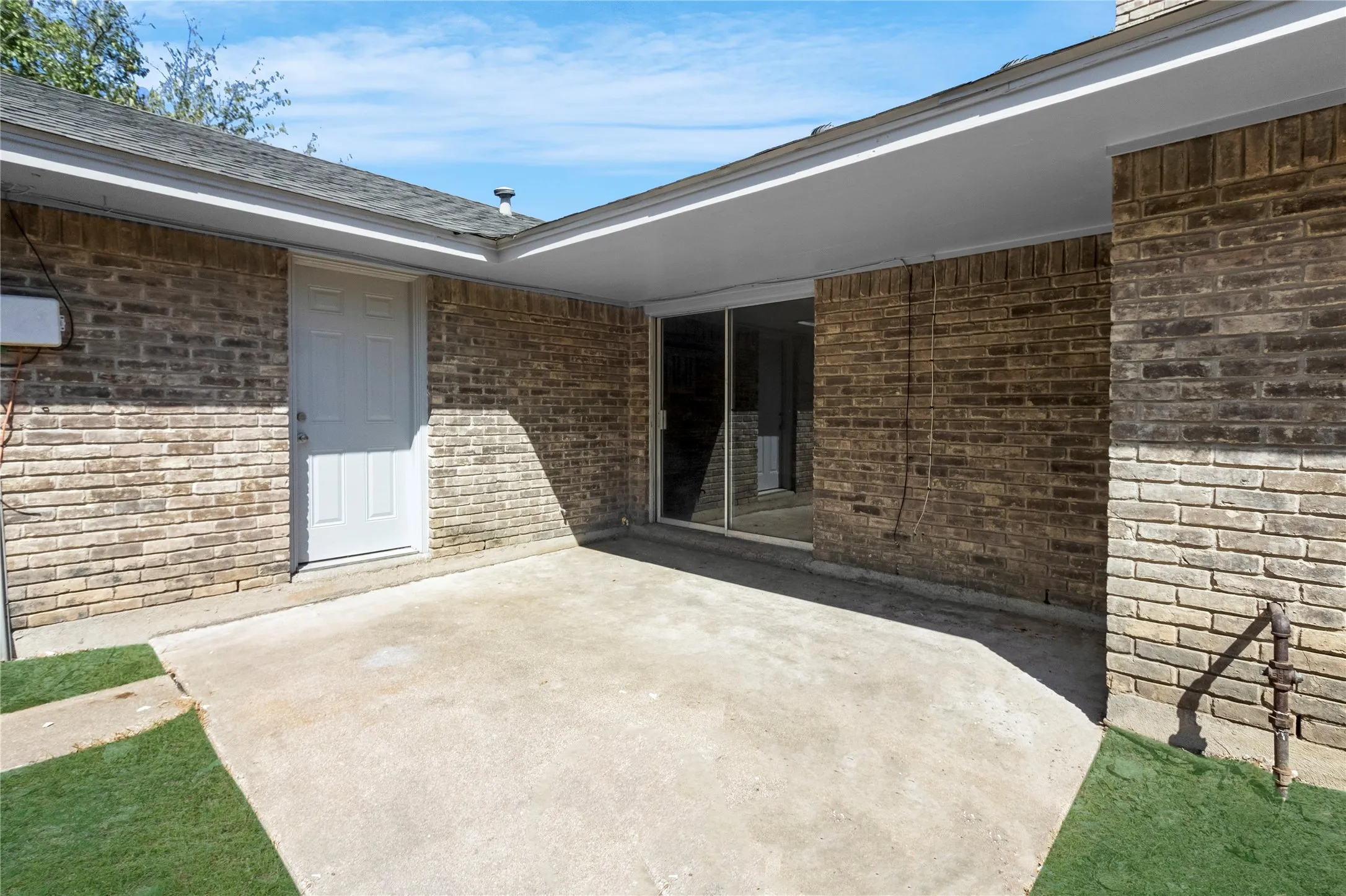 Concrete patio with brick exterior, covered overhang, sliding glass door, and exterior entry door