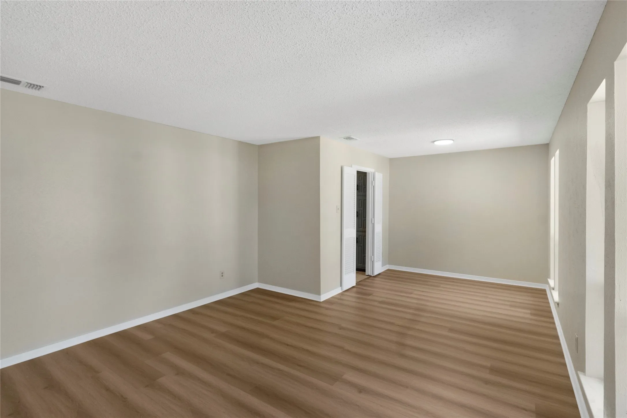 Spacious room featuring wood-finish flooring, light neutral wall tones, white trim, and a recessed ceiling light fixture