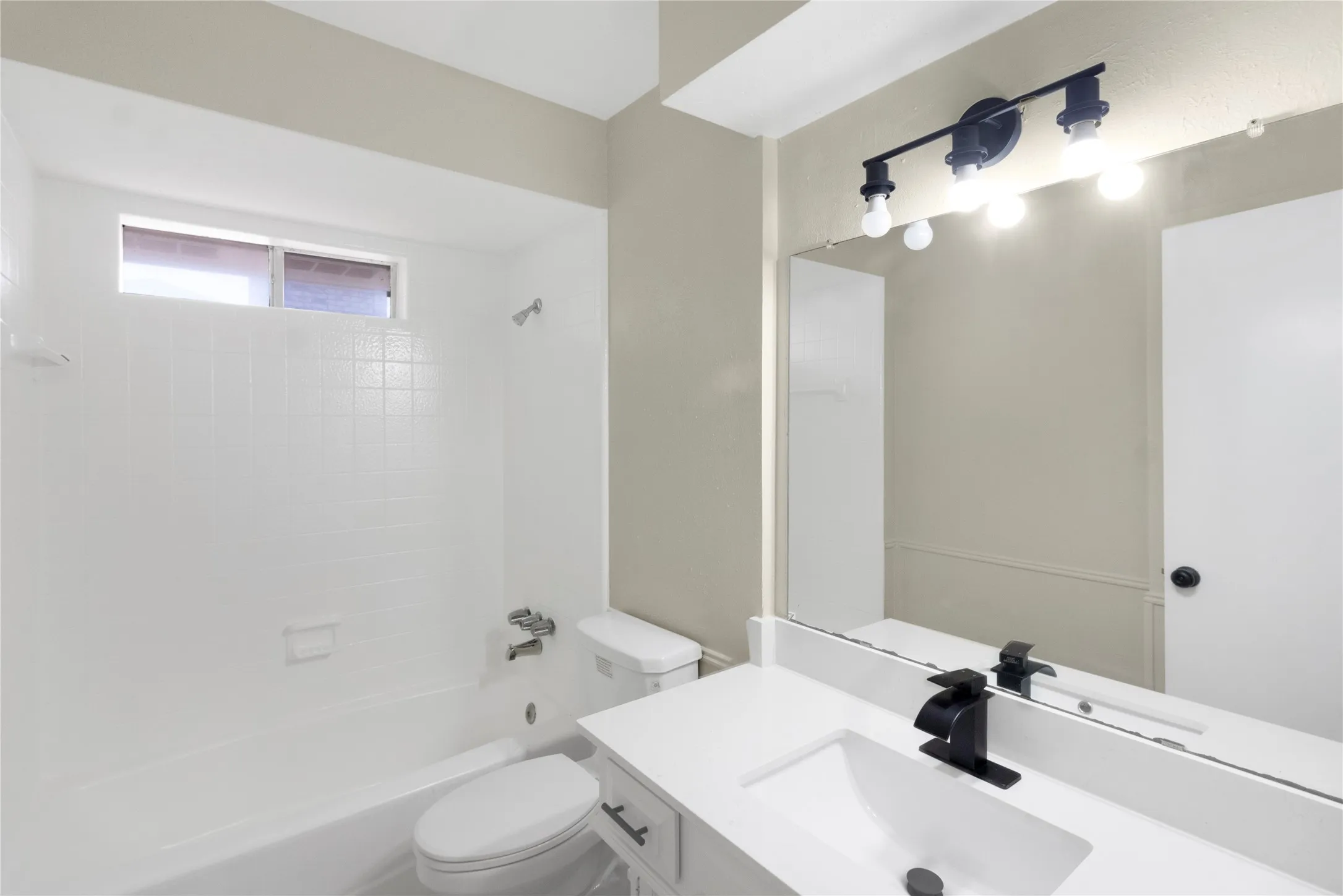 Bathroom featuring a white vanity with an integrated sink, black faucet, and a large mirror