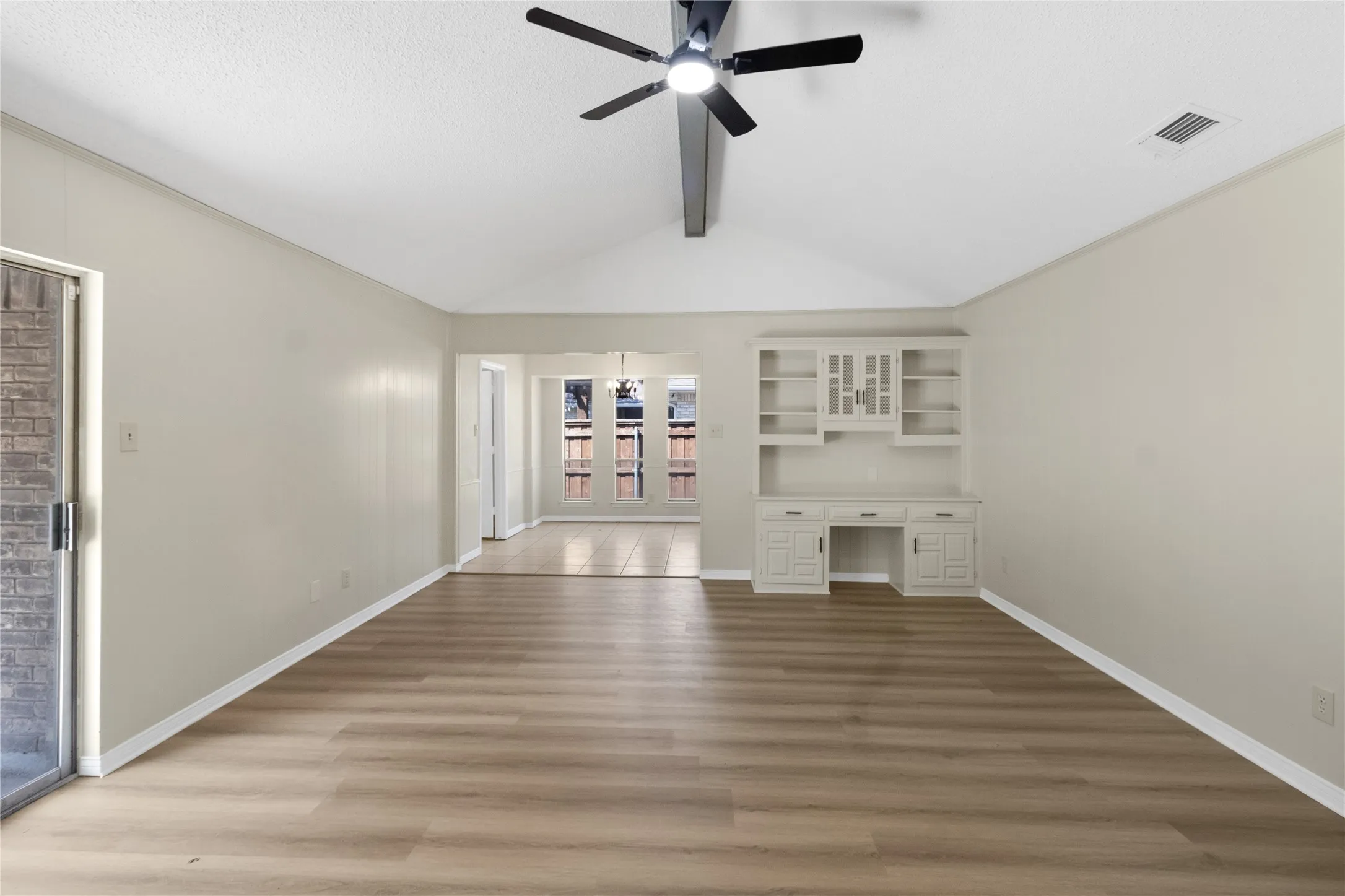 Vaulted ceiling with exposed beam, wood-finish flooring, built-in cabinetry, and a ceiling fan with integrated lighting