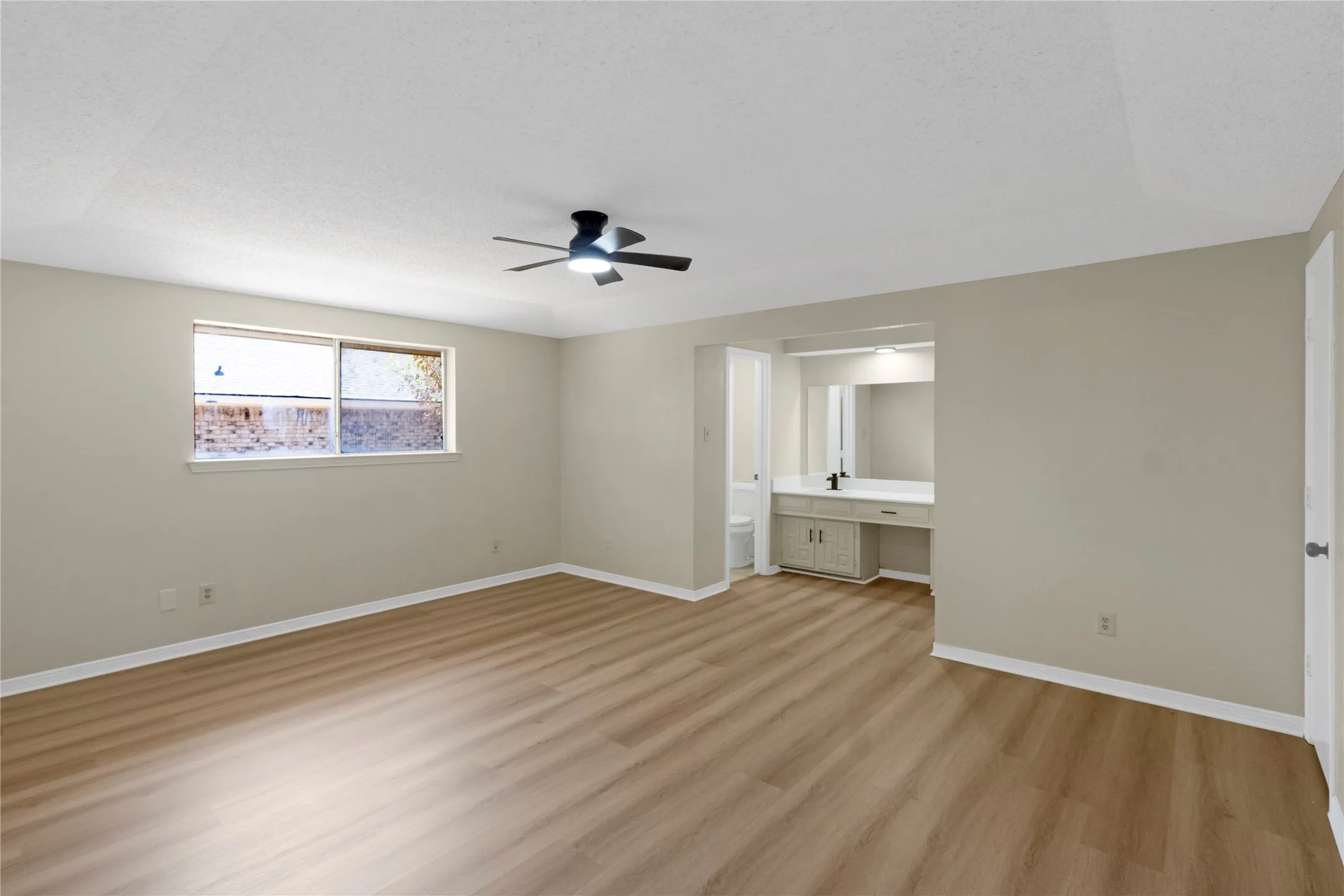 Wood-finish flooring, ceiling fan, vanity with integrated sink, and large mirror