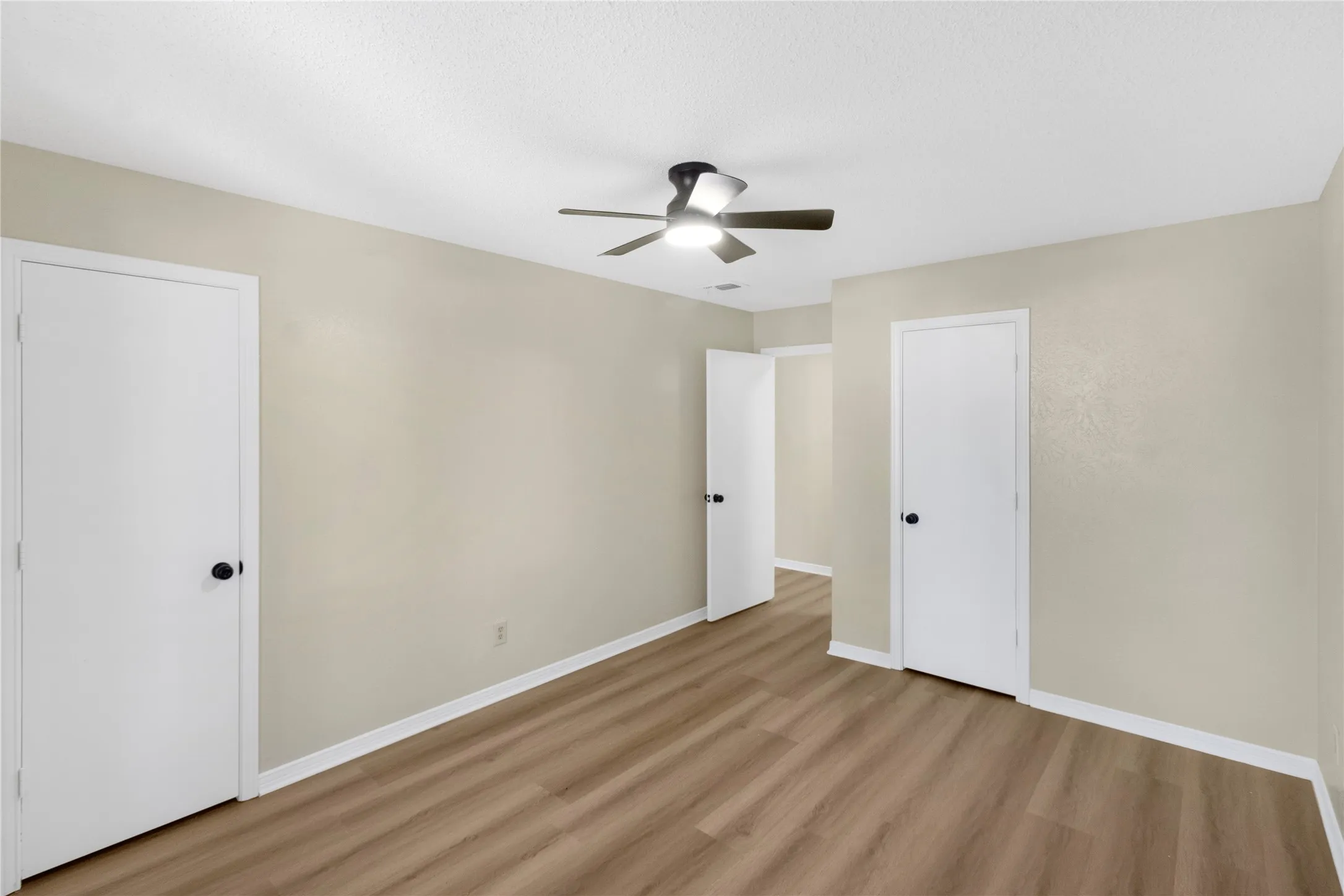 Neutral wall paint, wood-finish flooring, white trim, and a ceiling fan with integrated lighting