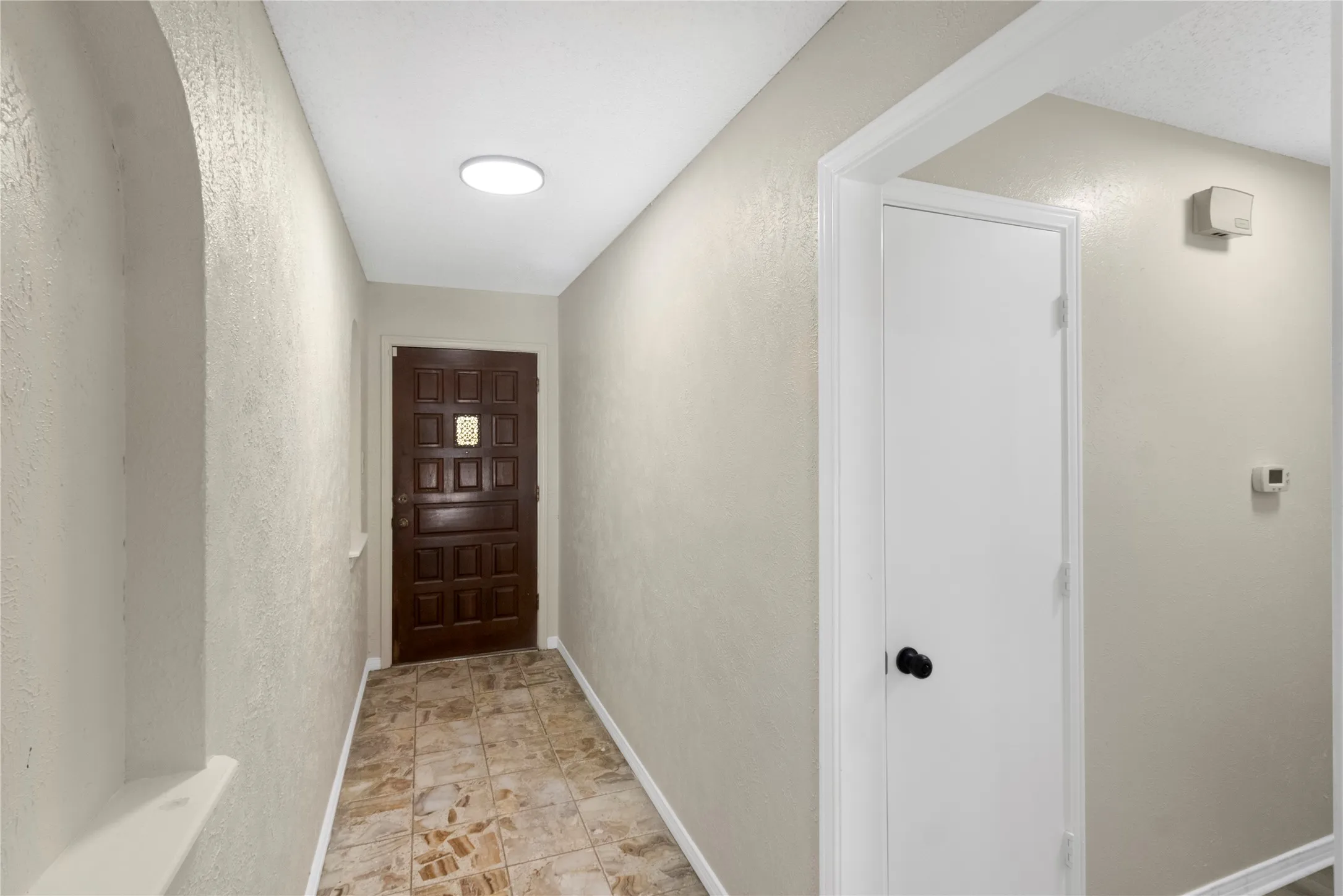 Textured wall finishes, brown paneled entry door, recessed ceiling lighting, tile flooring