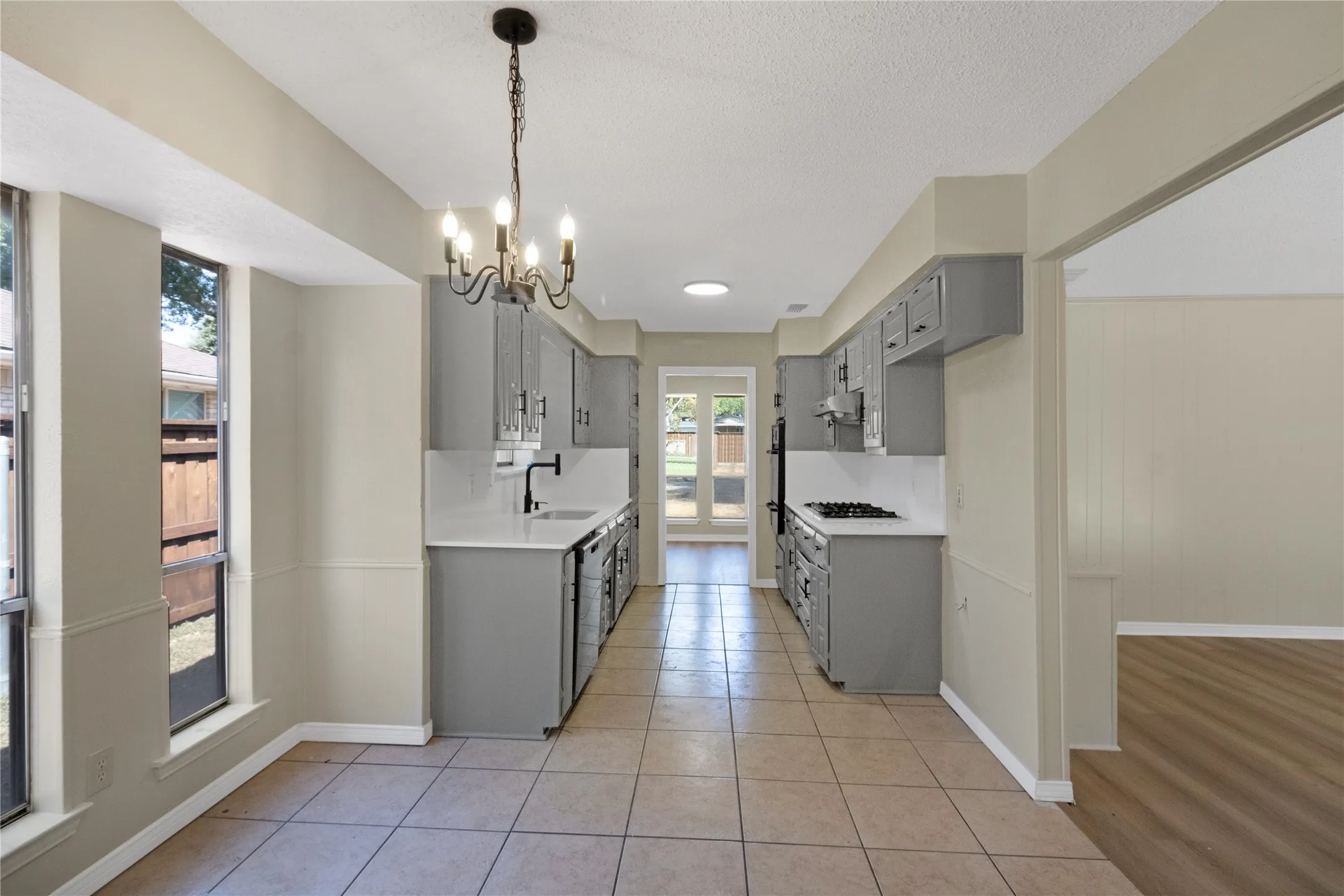Galley kitchen featuring tile flooring, gray cabinetry, white countertops, and a black cooktop