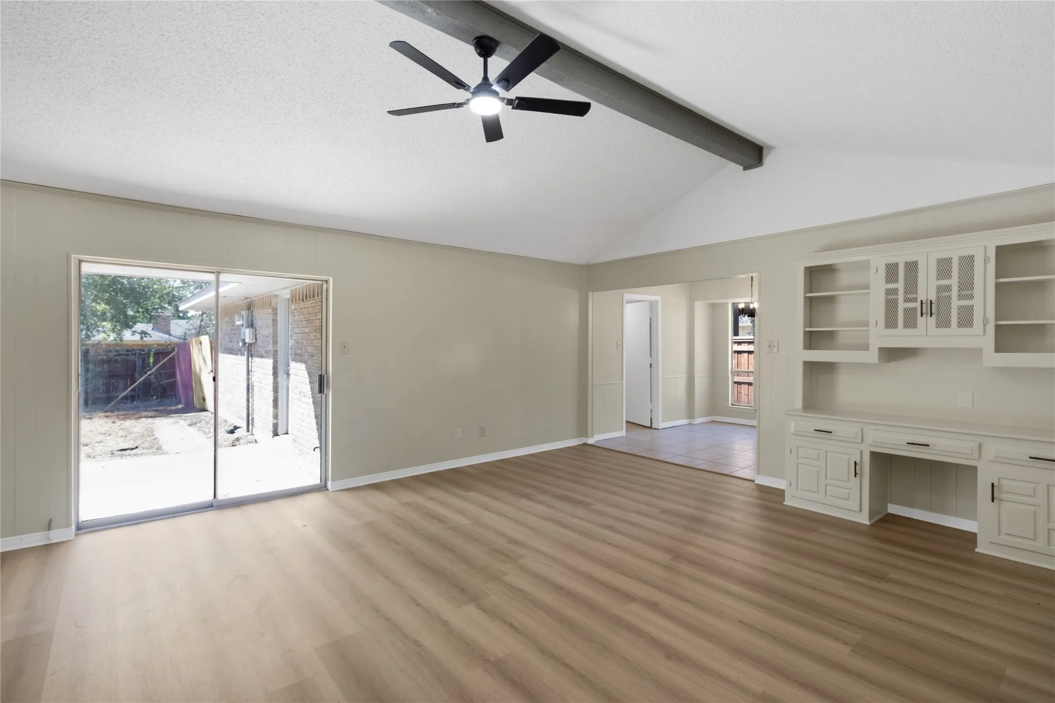 Vaulted ceiling with an exposed beam, wood-finish flooring, built-in cabinetry, and sliding glass​​‌​​​​‌​​‌‌​‌‌​​​‌‌​‌​‌​‌​​​‌​​ doors