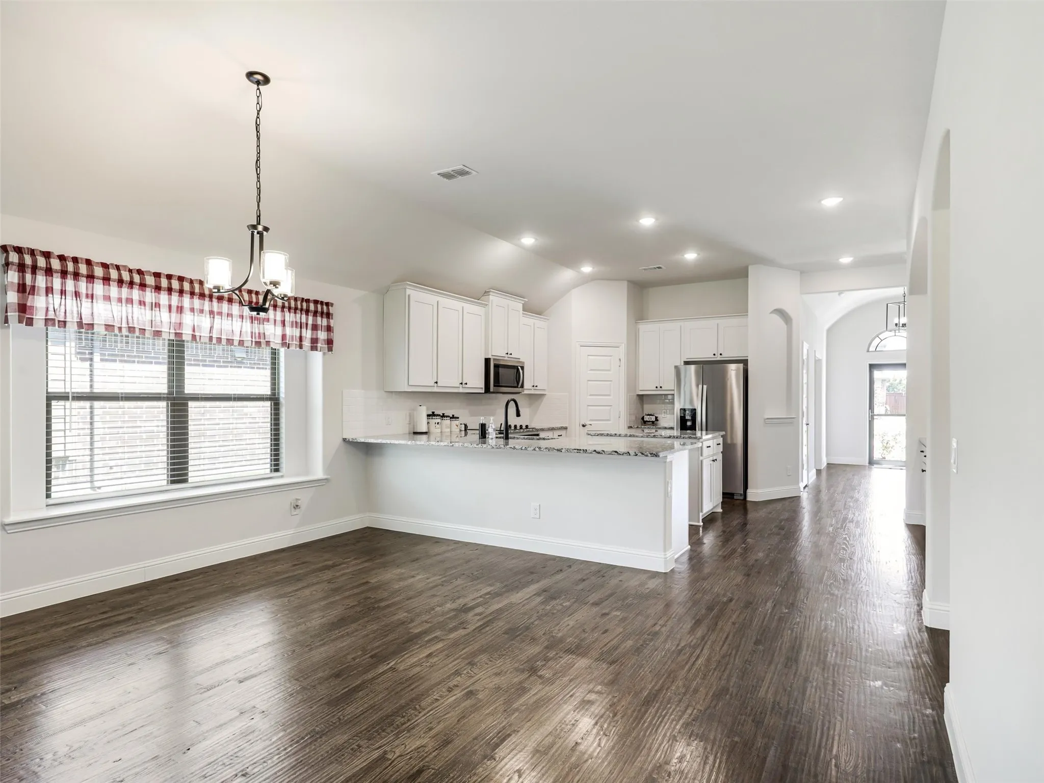 Open-concept kitchen and dining area featuring wood-finish flooring, white cabinetry, recessed lighting, and a stainless steel refrigerator
