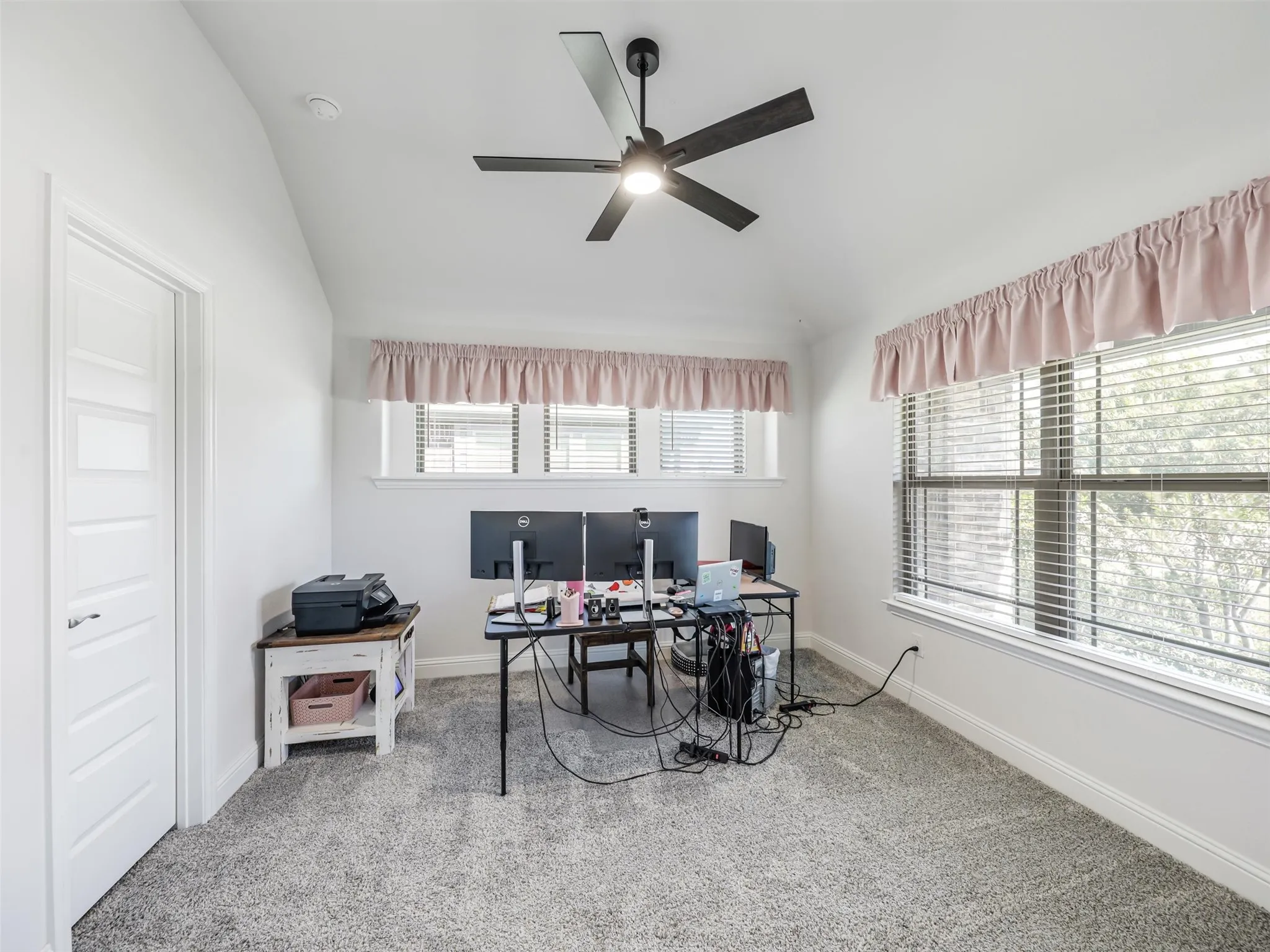 Vaulted ceiling with a ceiling fan, light gray carpet, and multiple windows providing natural illumination