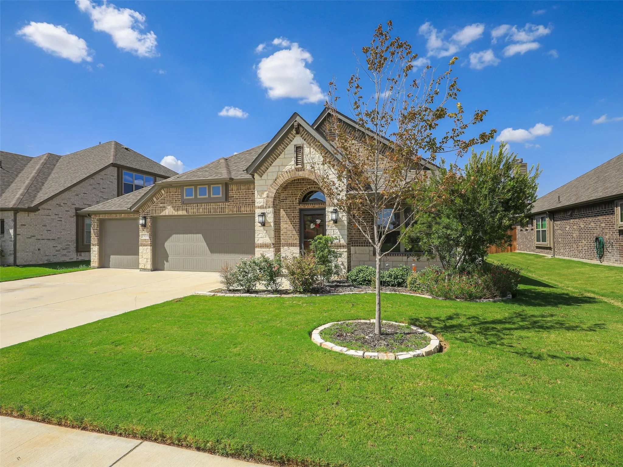 Brick and stone facade, arched entryway, two-car garage, established landscaping, and a well-maintained lawn