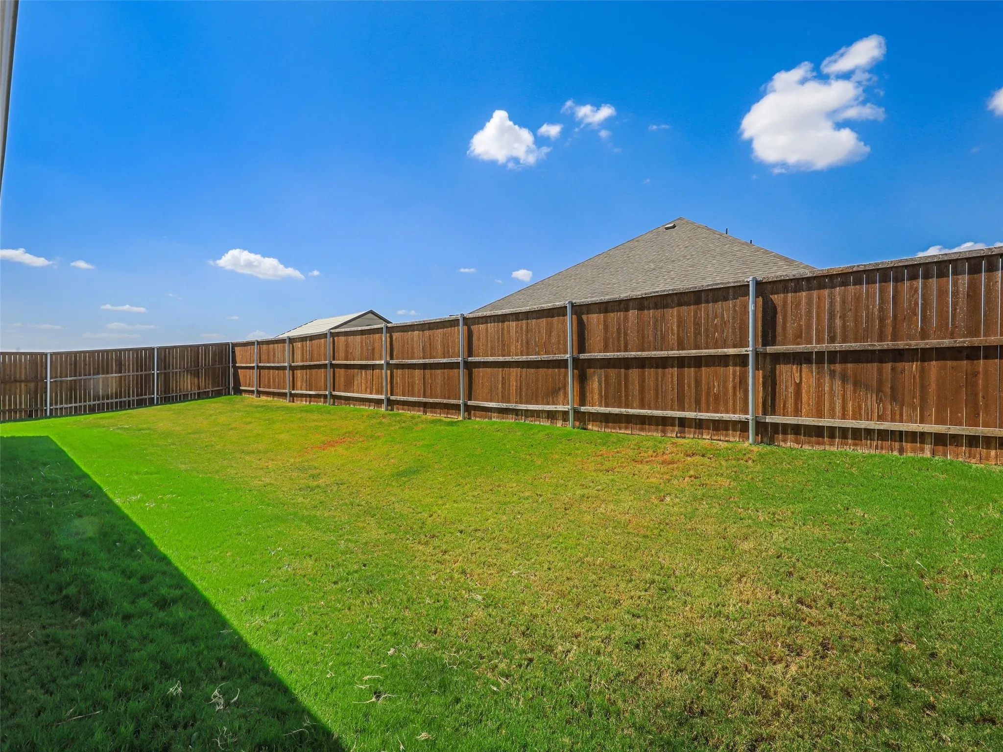 Expansive backyard featuring a manicured lawn, full wood privacy fencing, and a visible building structure