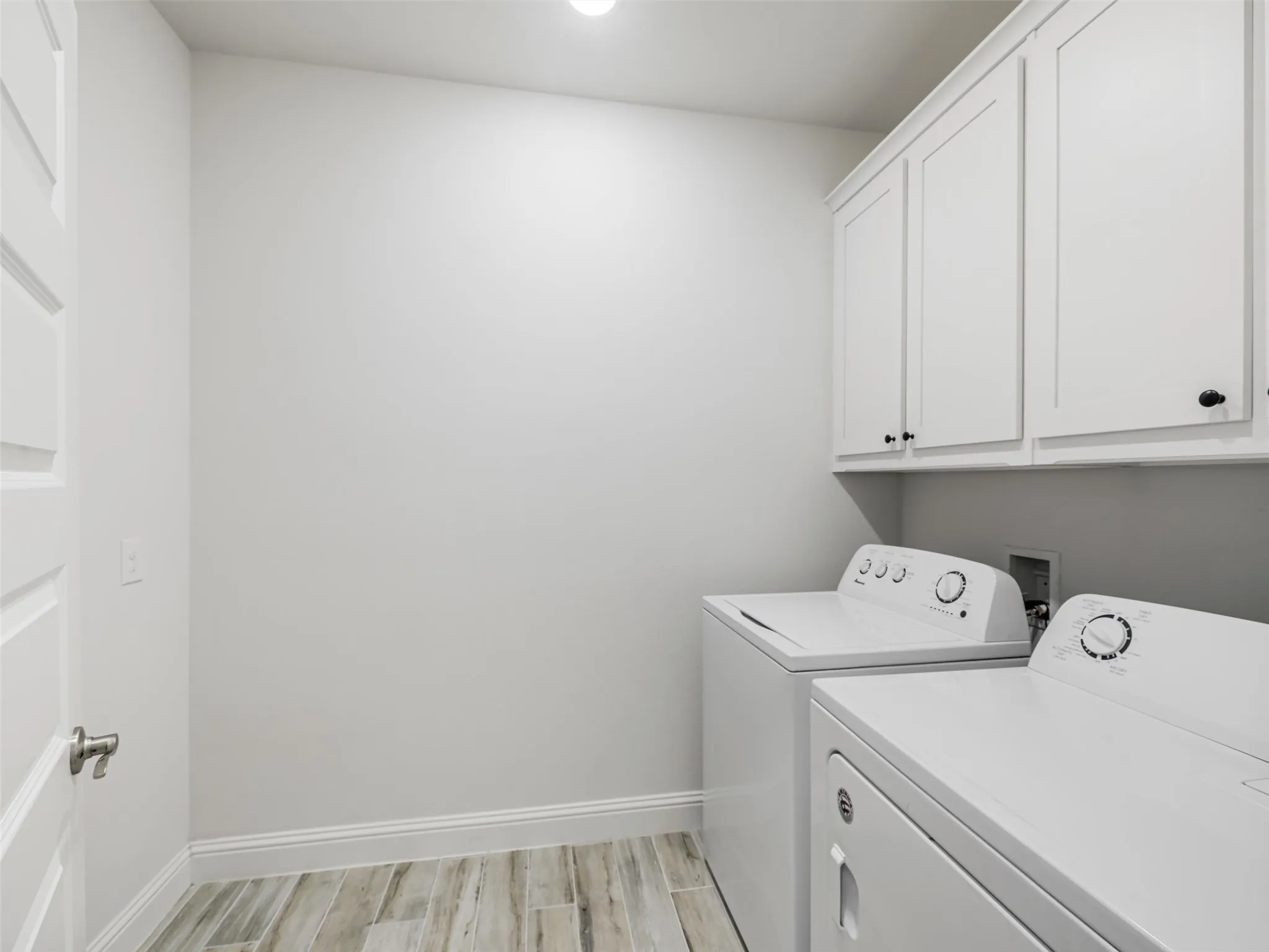 Laundry area featuring wood-finish flooring, white shaker-style cabinetry, and recessed lighting