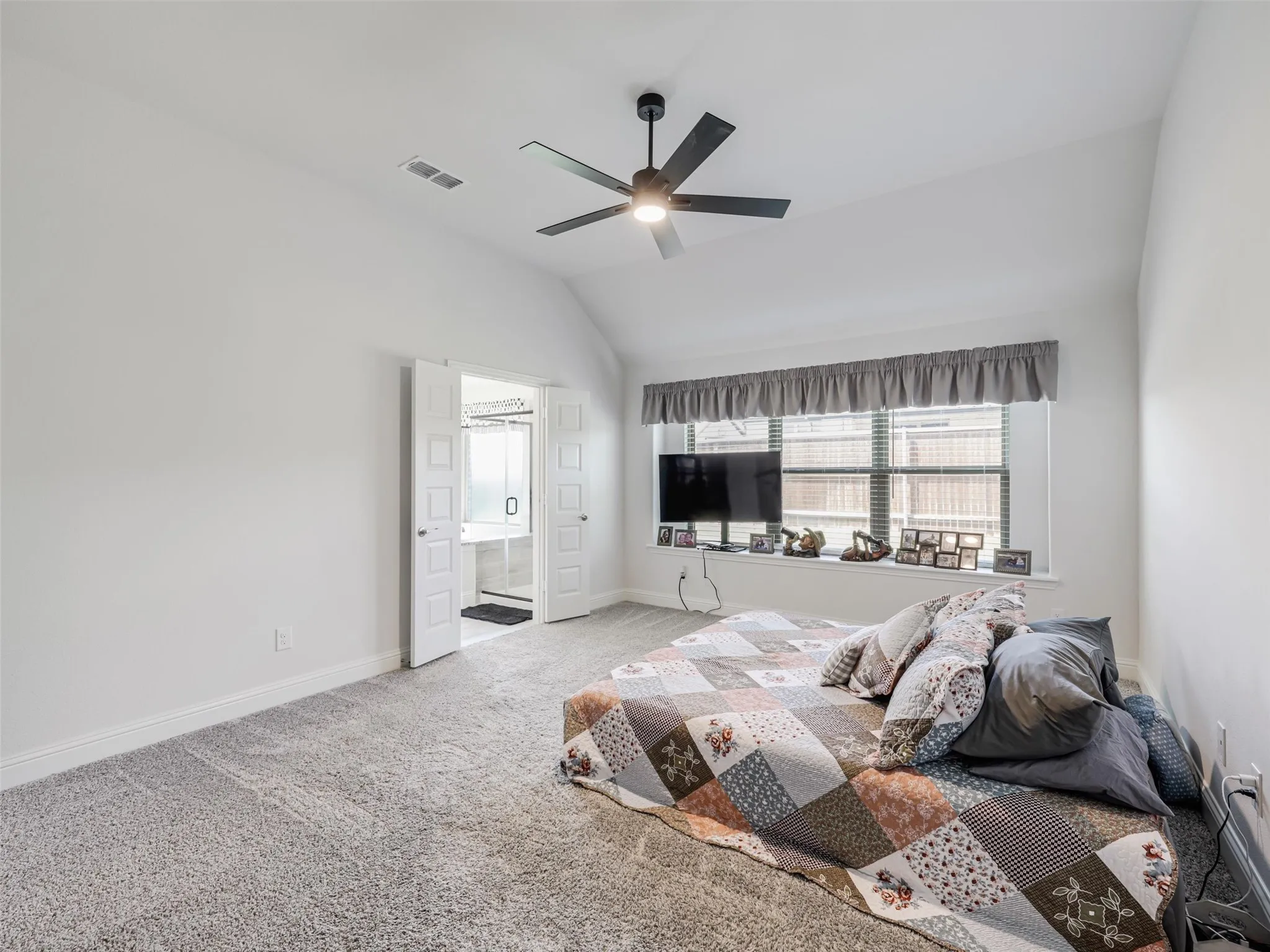 Vaulted ceiling with a contemporary ceiling fan, light gray carpeting, and a wide window with blinds