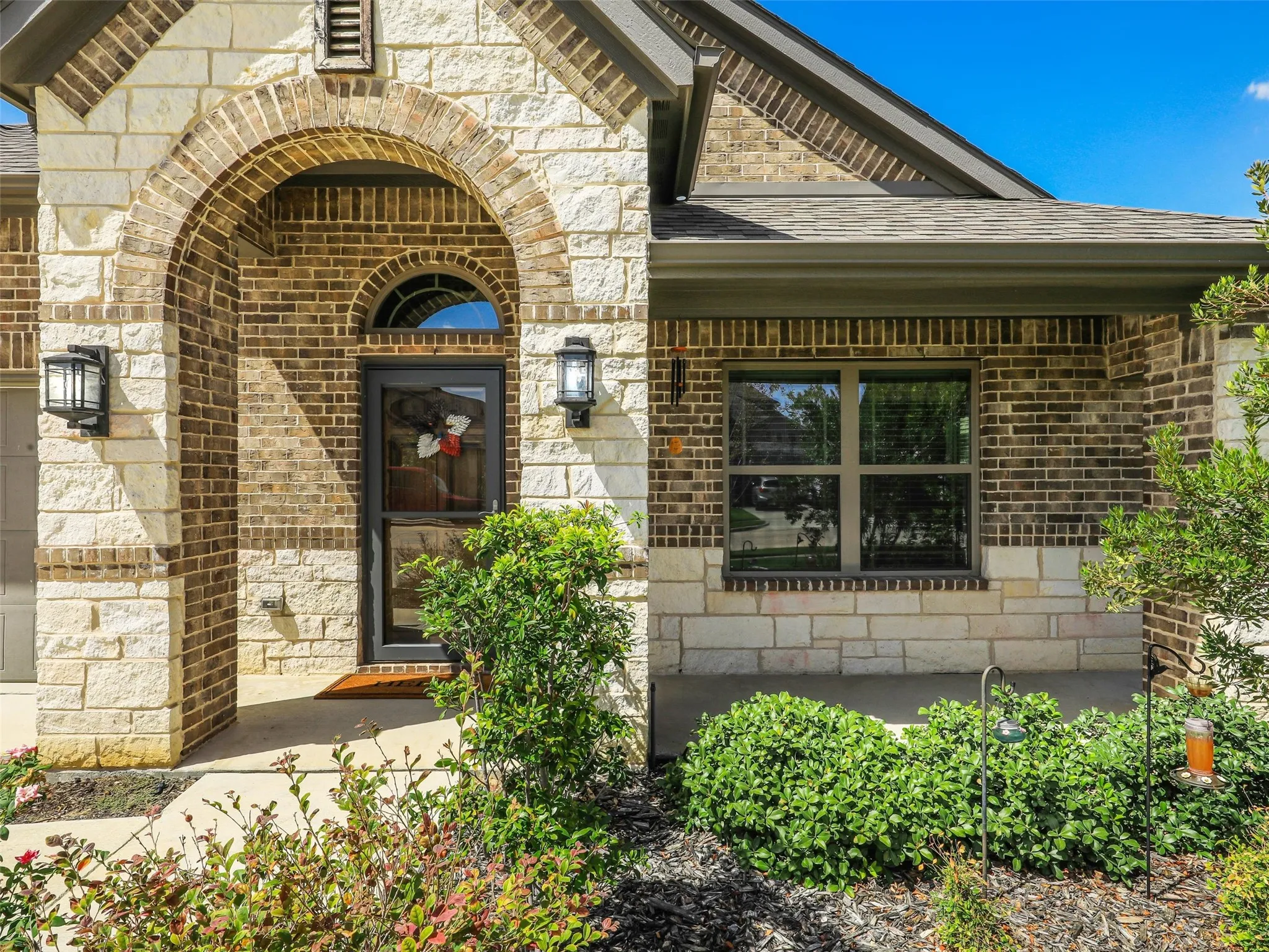 Brick and stone exterior with an arched entryway, transom window, and dual wall-mounted lanterns