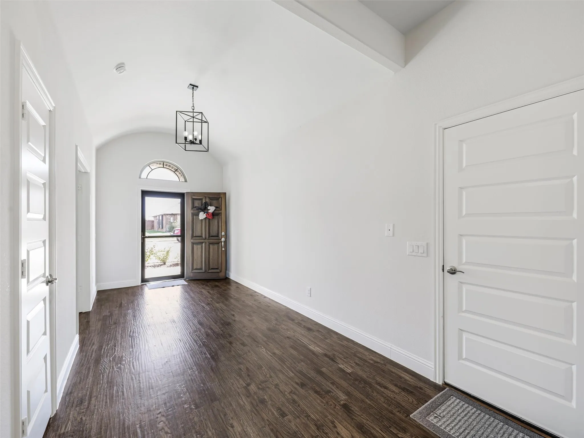 Vaulted ceiling with a contemporary black metal chandelier, dark wood-finish flooring, and a solid wood entry door with an arched transom window