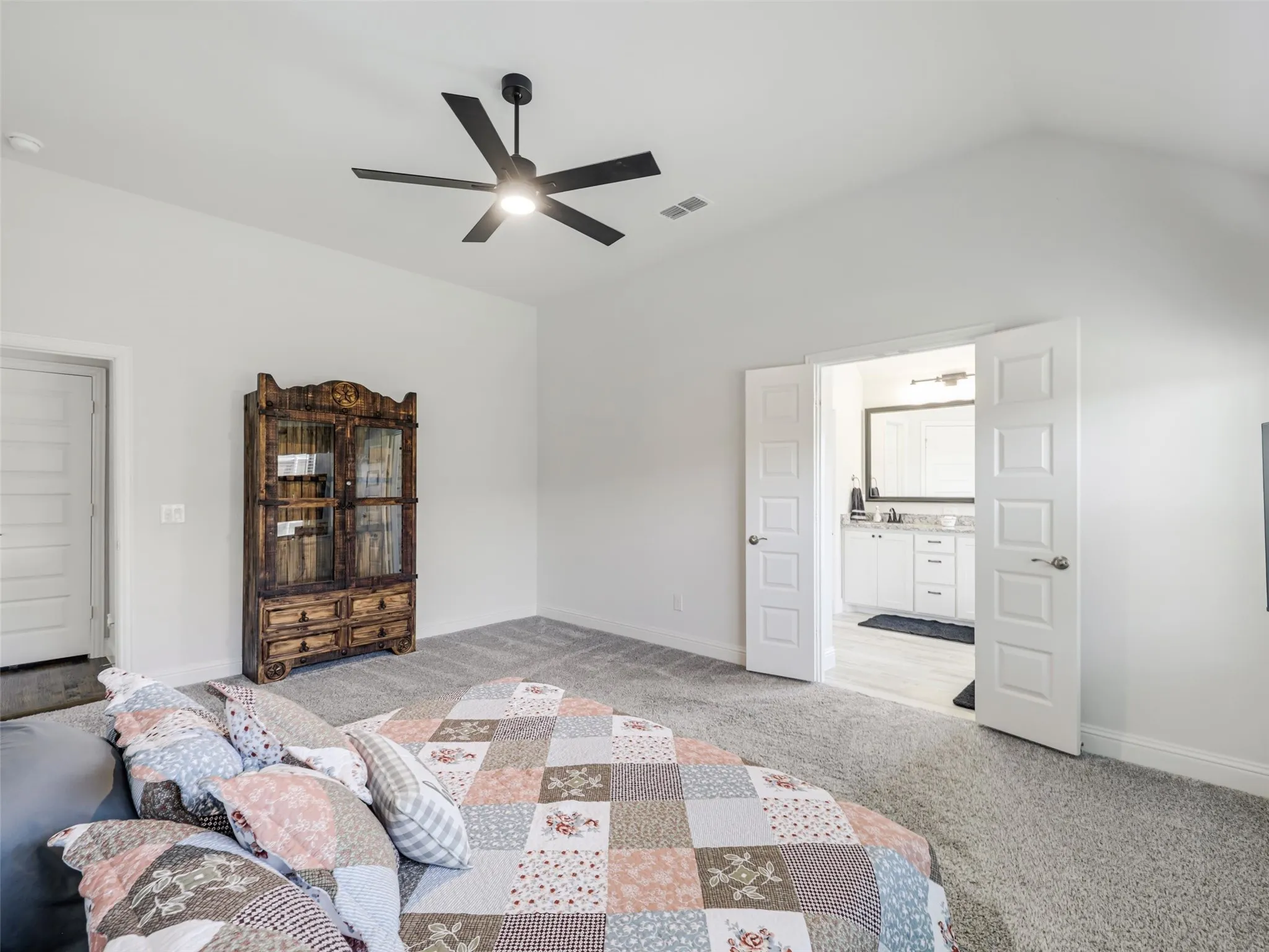 Vaulted ceiling with a ceiling fan, plush carpet flooring, and white double doors opening to a bathroom with a vanity