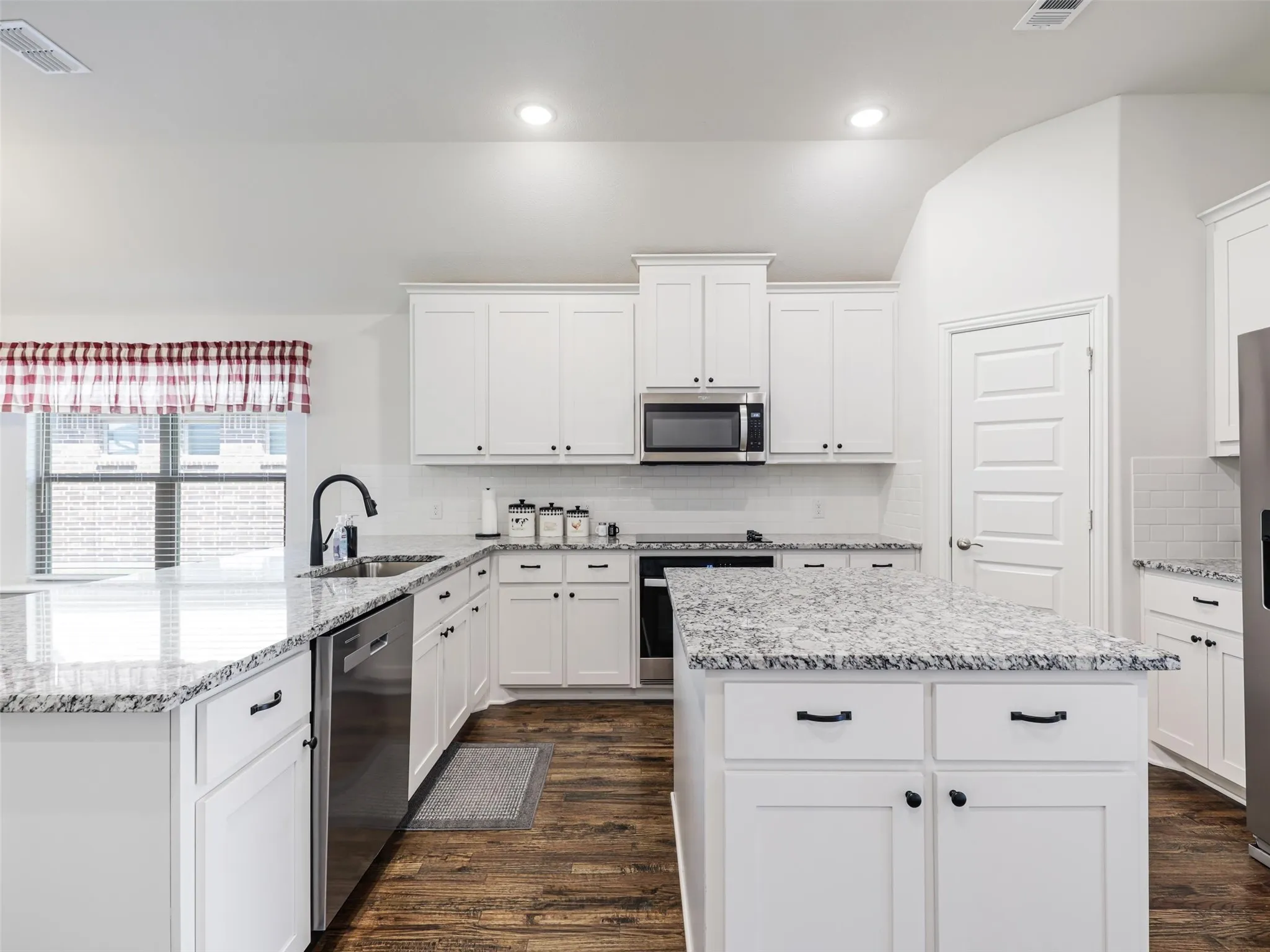 Kitchen featuring white shaker-style cabinetry, granite countertops, stainless steel appliances, and wood-finish flooring